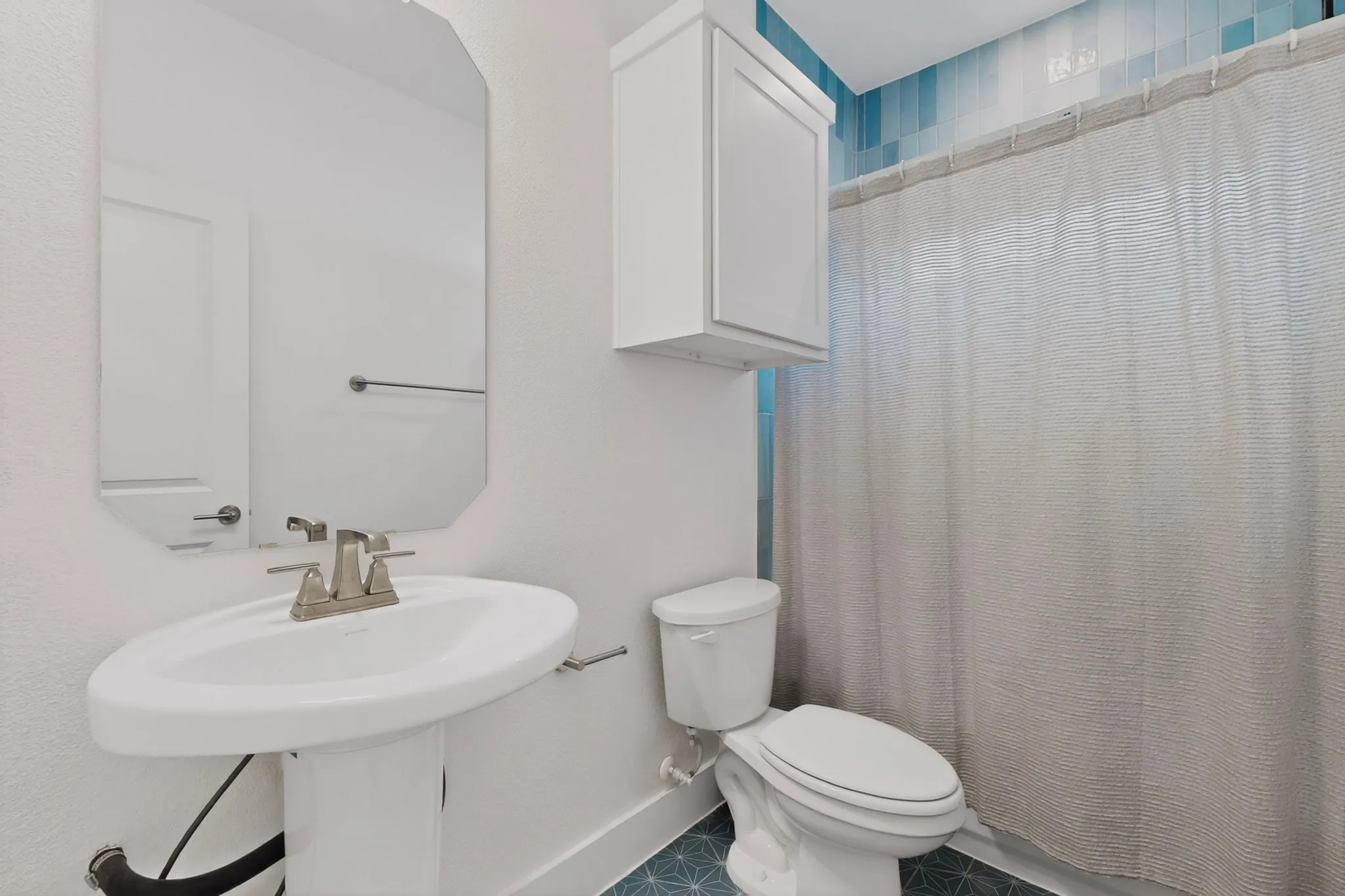 Bathroom featuring a pedestal sink, brushed nickel faucet, wall-mounted mirror, and cabinet storage
