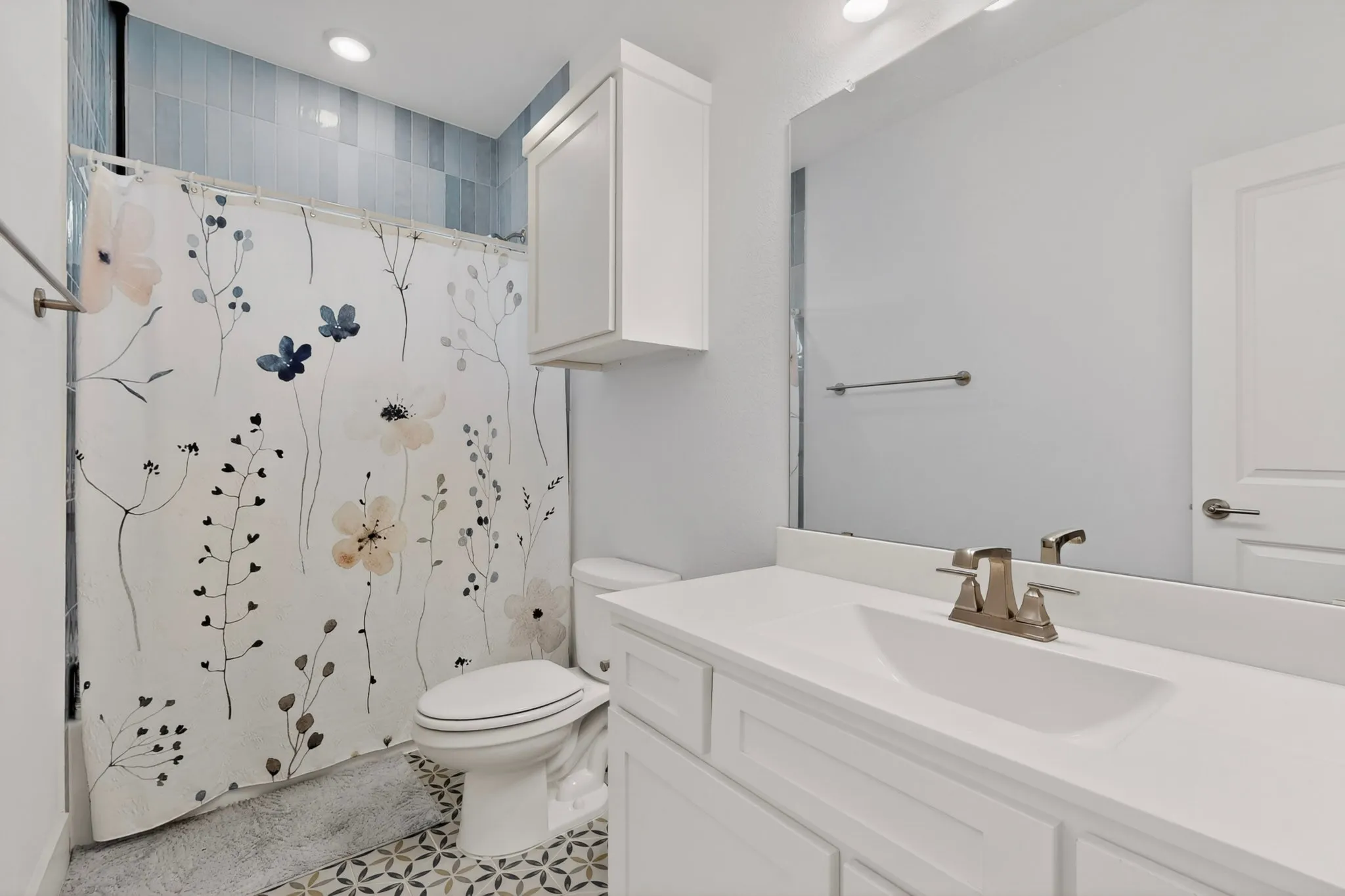 Bathroom featuring patterned floor tiling, a white vanity with integrated sink, and an overhead storage cabinet