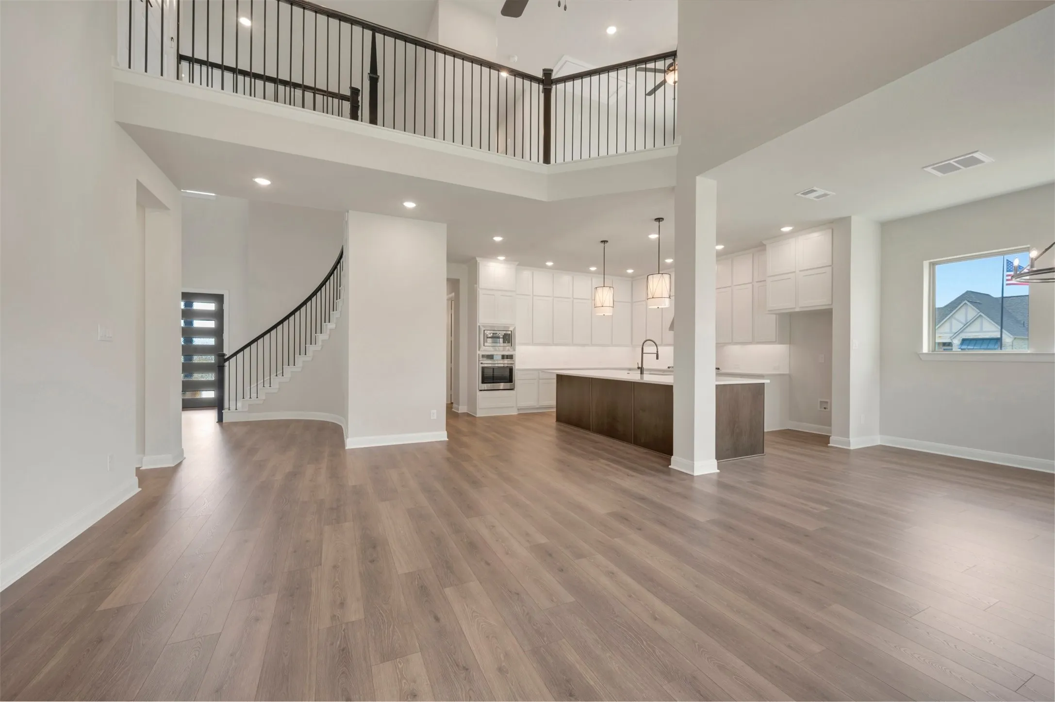Open-concept living area featuring wood-finish flooring, a two-story foyer, a grand curved staircase, a spacious kitchen island, and contemporary pendant lighting