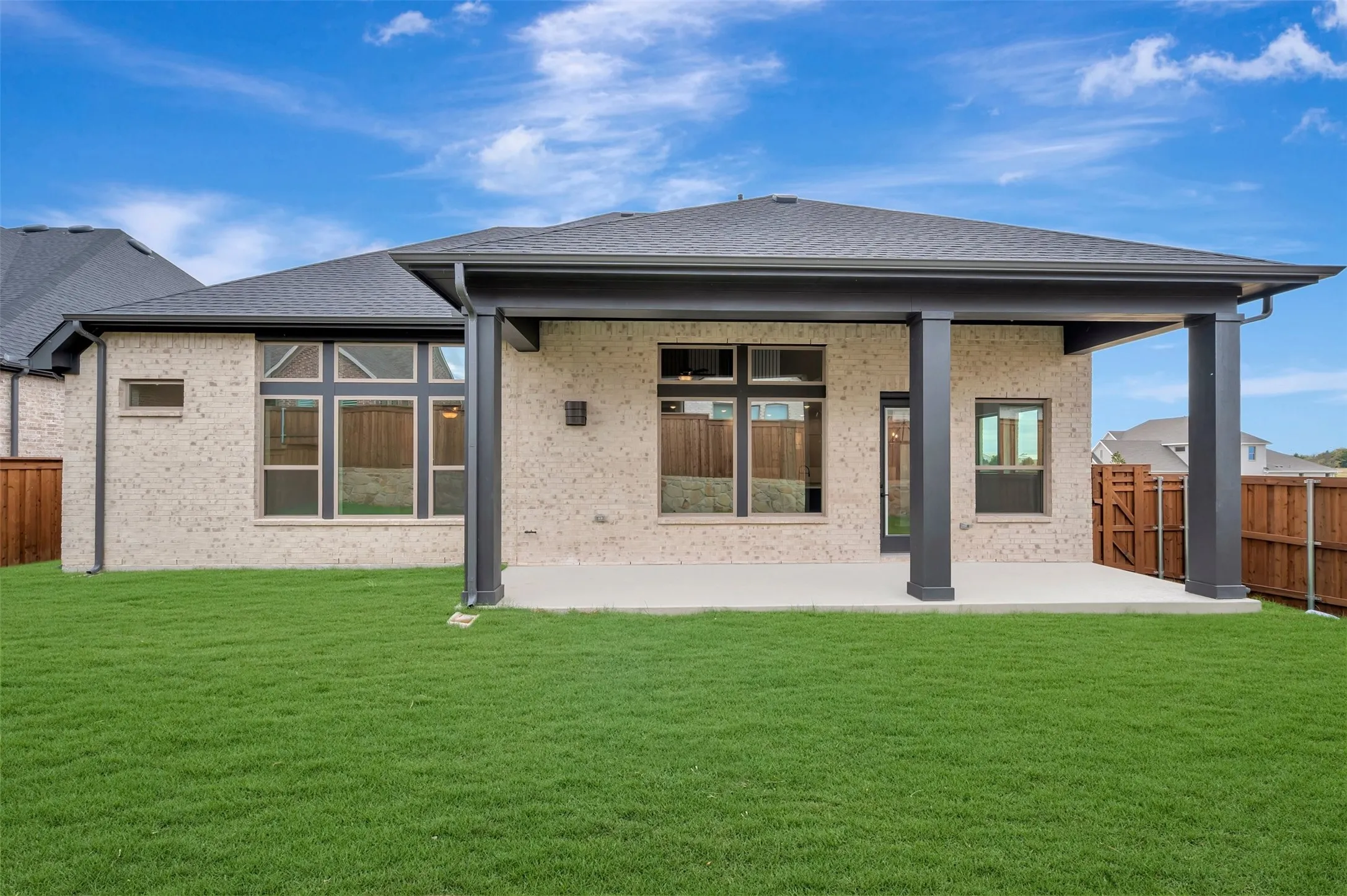 Expansive backyard featuring a lush lawn, a covered patio with dark columns, and a brick exterior with multiple windows