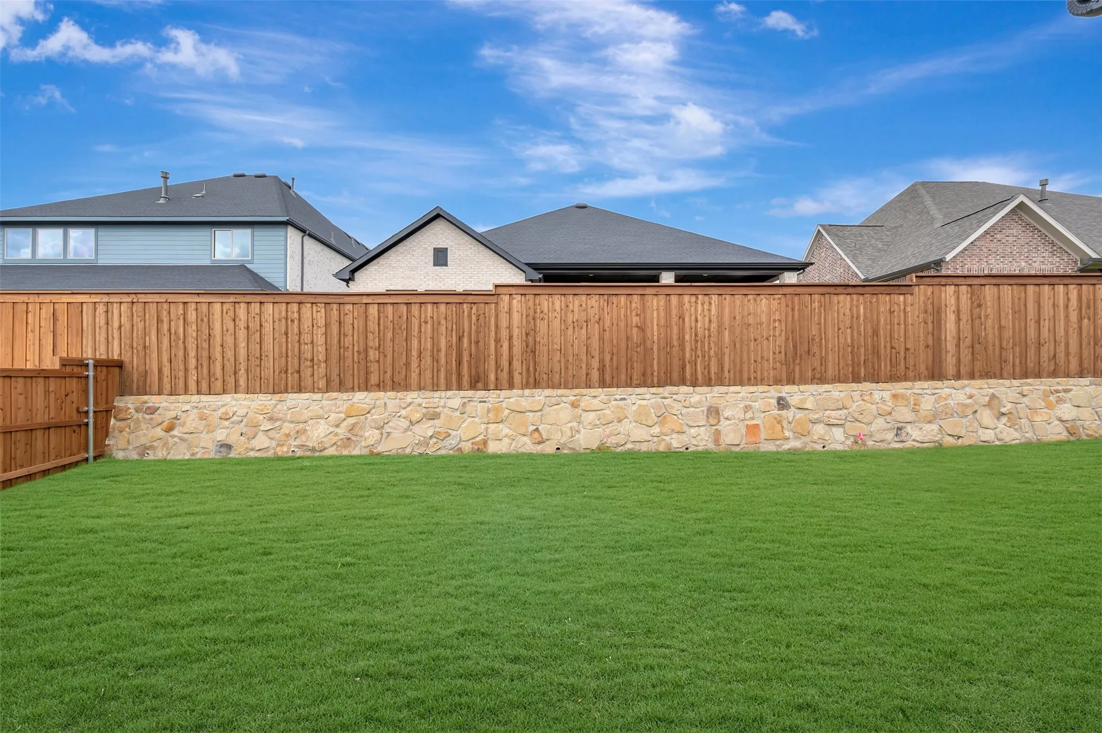 Expansive lawn area with a stone retaining wall and a wood privacy fence