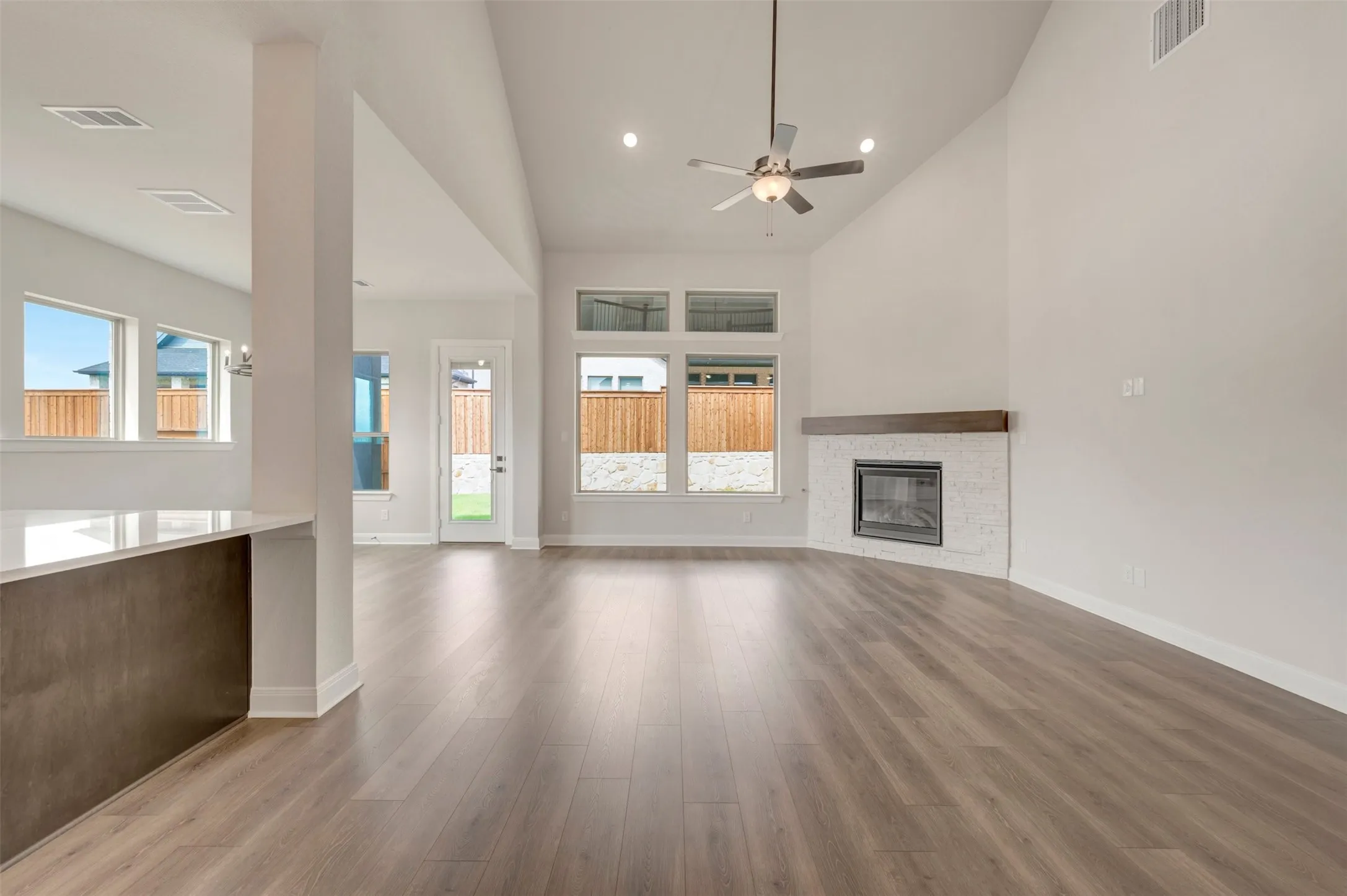 Vaulted ceiling with a ceiling fan, wood-finish flooring, fireplace with a tiled surround and wood mantel, large windows, and a glass-paneled door