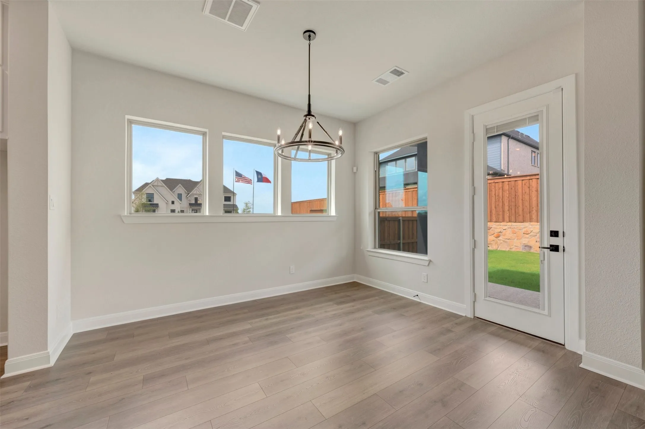 Wood-finish flooring, a contemporary chandelier, multiple windows, and a glass-paneled door