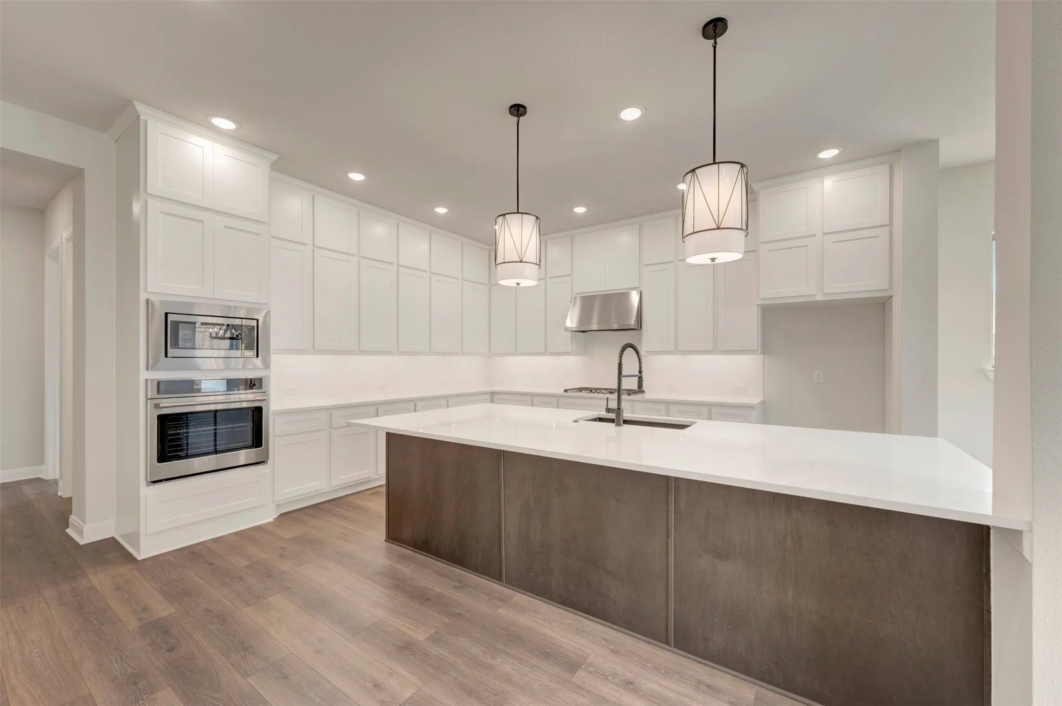 Expansive kitchen featuring white cabinetry, a large center island, stainless steel appliances, pendant lighting, and wood-finish flooring