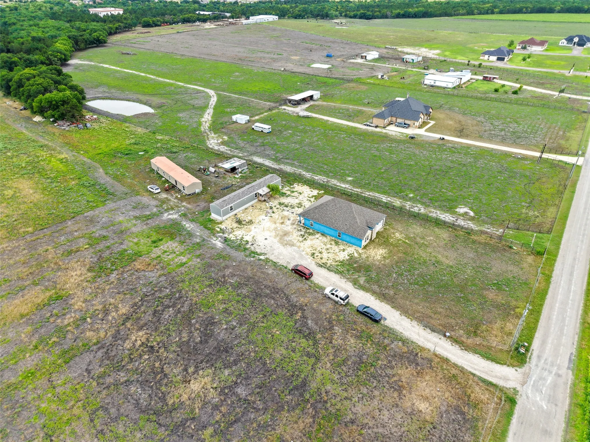 Expansive land parcel featuring a blue-sided structure with a gray shingle roof, accompanied by two long, light-colored outbuildings
