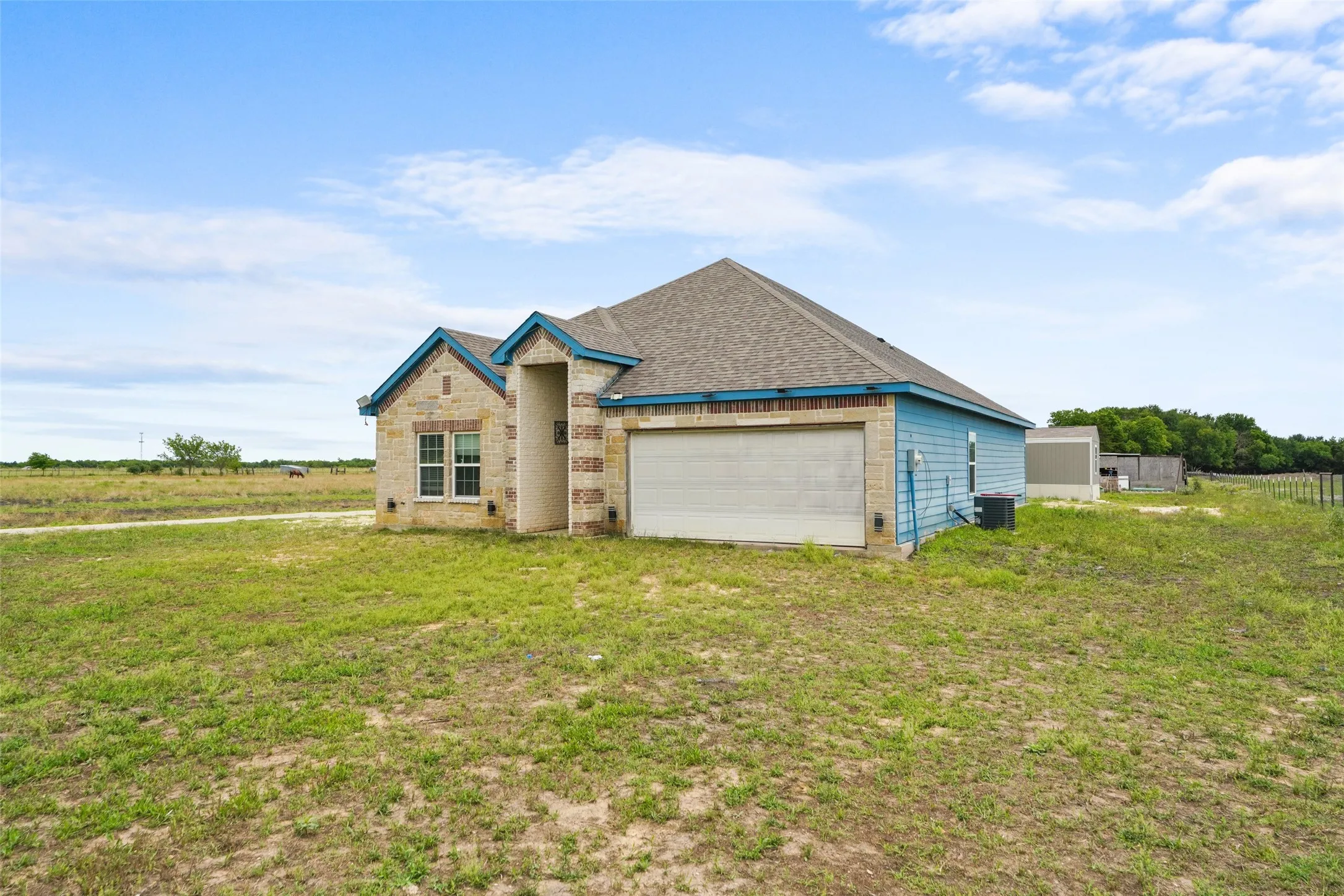 Exterior featuring a stone facade and light blue siding, a multi-pitched roofline, an attached garage, and a spacious grassy yard