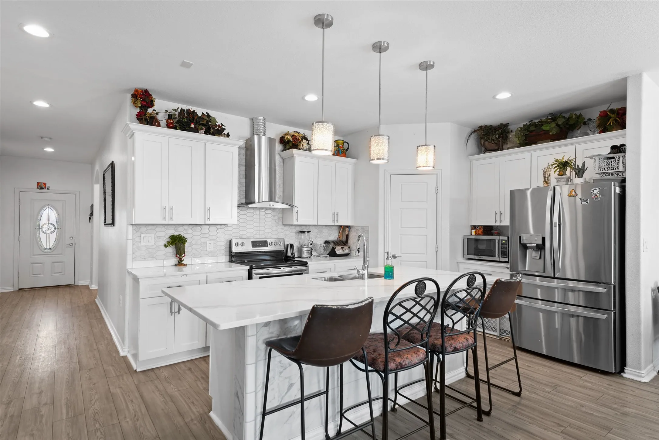 Open-concept kitchen with white cabinetry, stainless steel appliances, a center island with pendant lighting, and wood-finish flooring