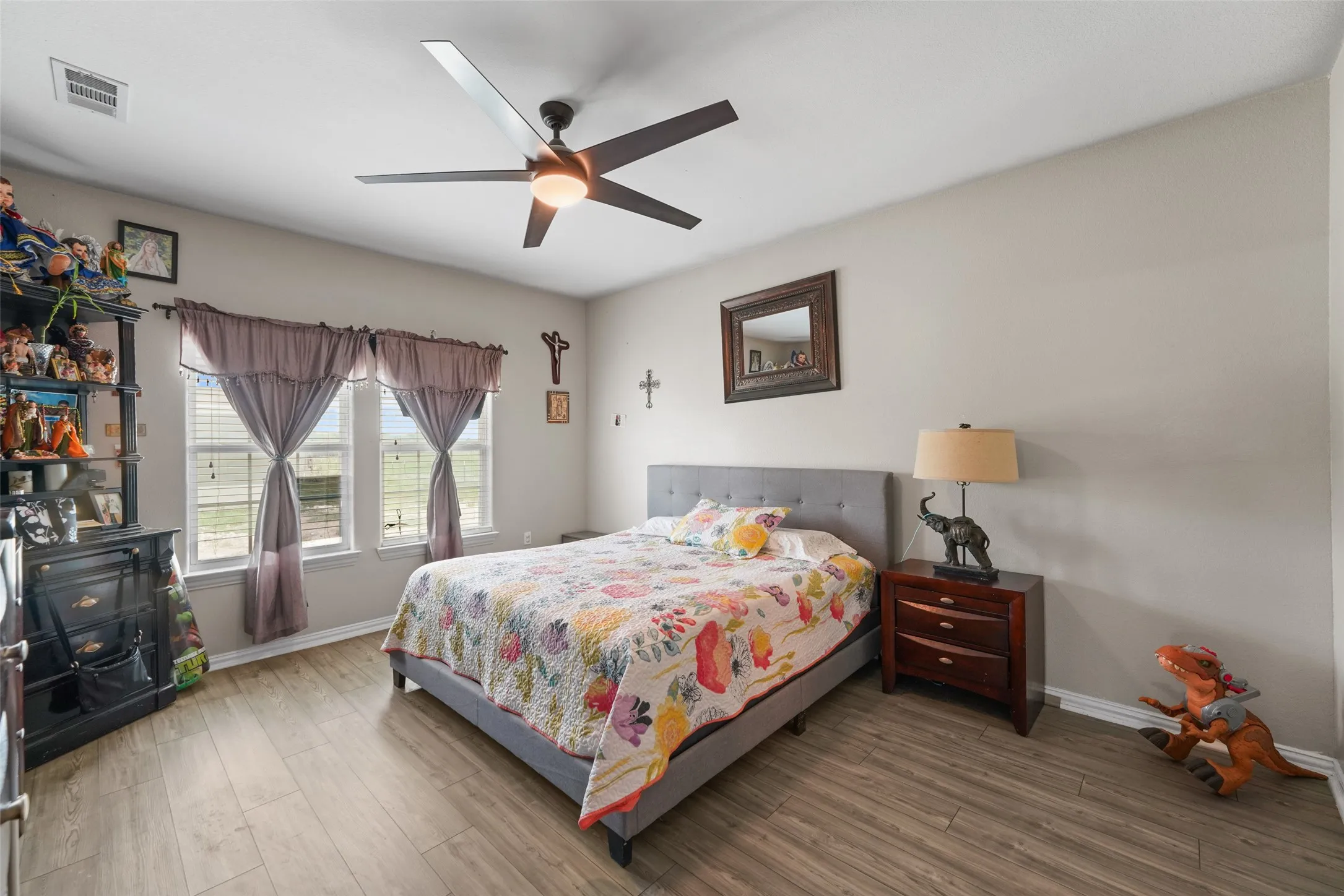 Bedroom featuring wood-finish flooring, a contemporary ceiling fan with integrated lighting, and multiple windows for natural light