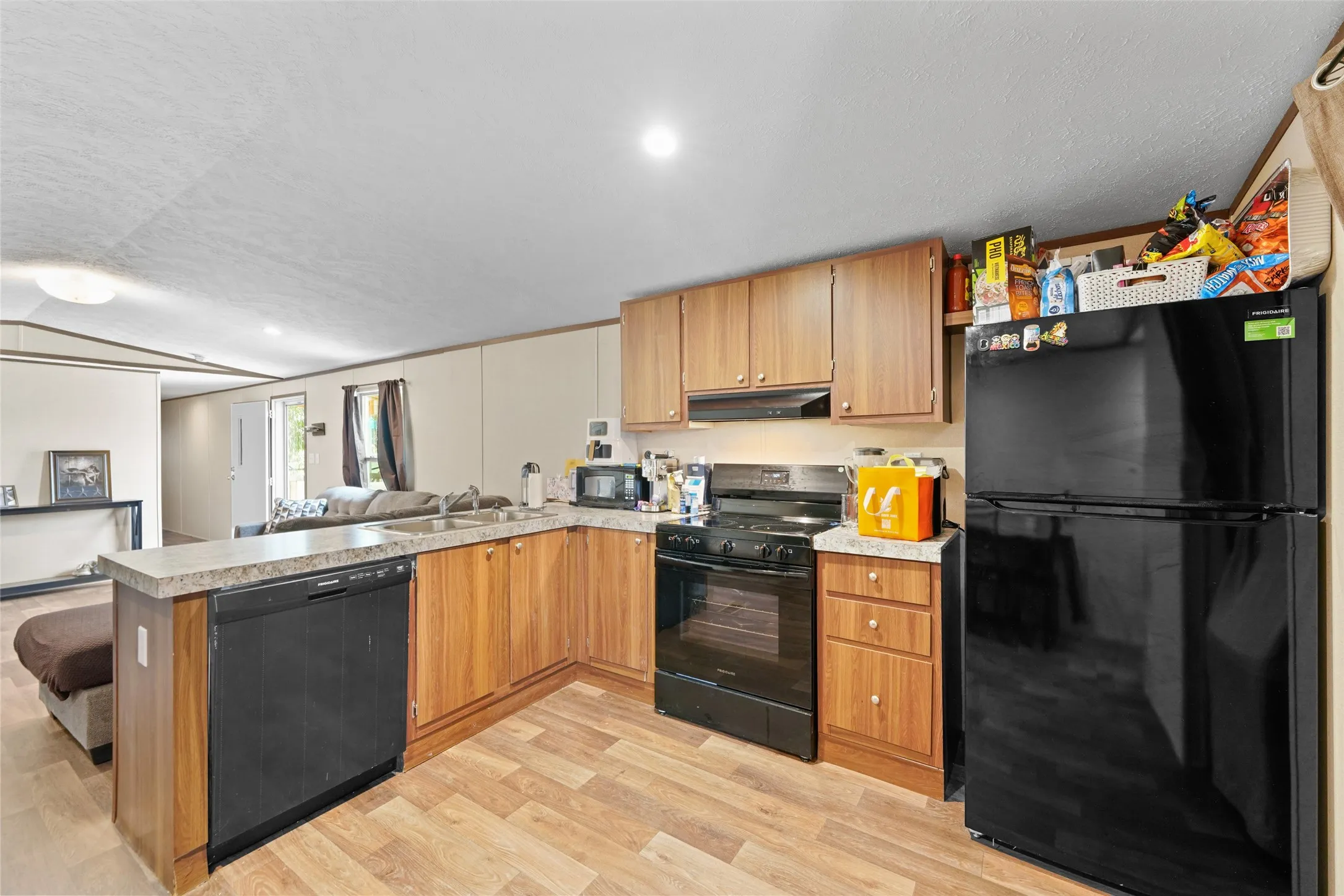 U-shaped kitchen featuring wood-finish cabinetry, a black appliance suite, and light-toned countertops