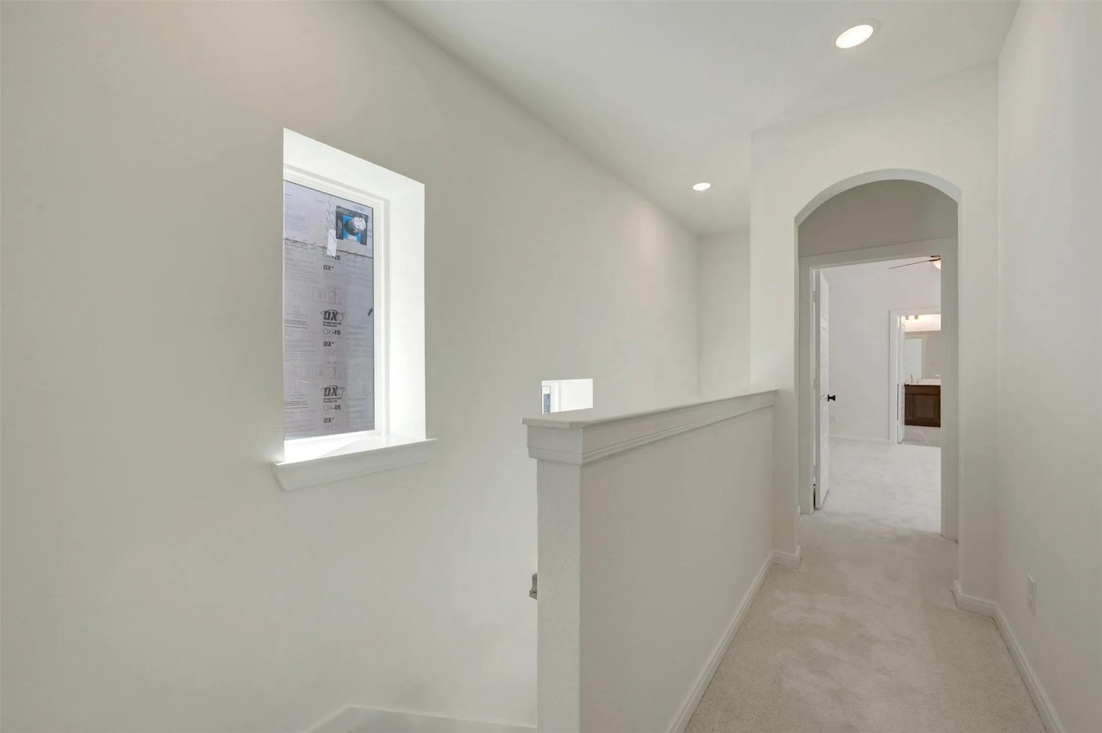 Carpeted hallway with an arched doorway, recessed lighting, and a window