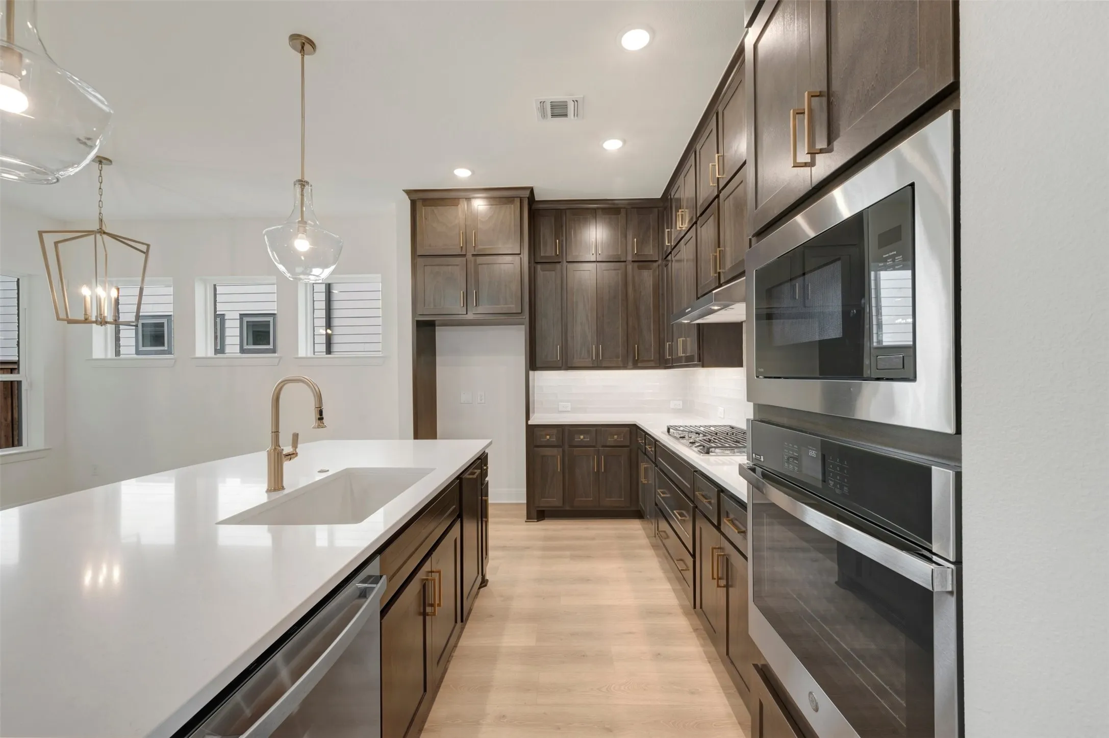 Open-concept kitchen featuring an expansive island with an integrated sink, custom dark wood cabinetry, white subway tile backsplash, and stainless steel built-in appliances