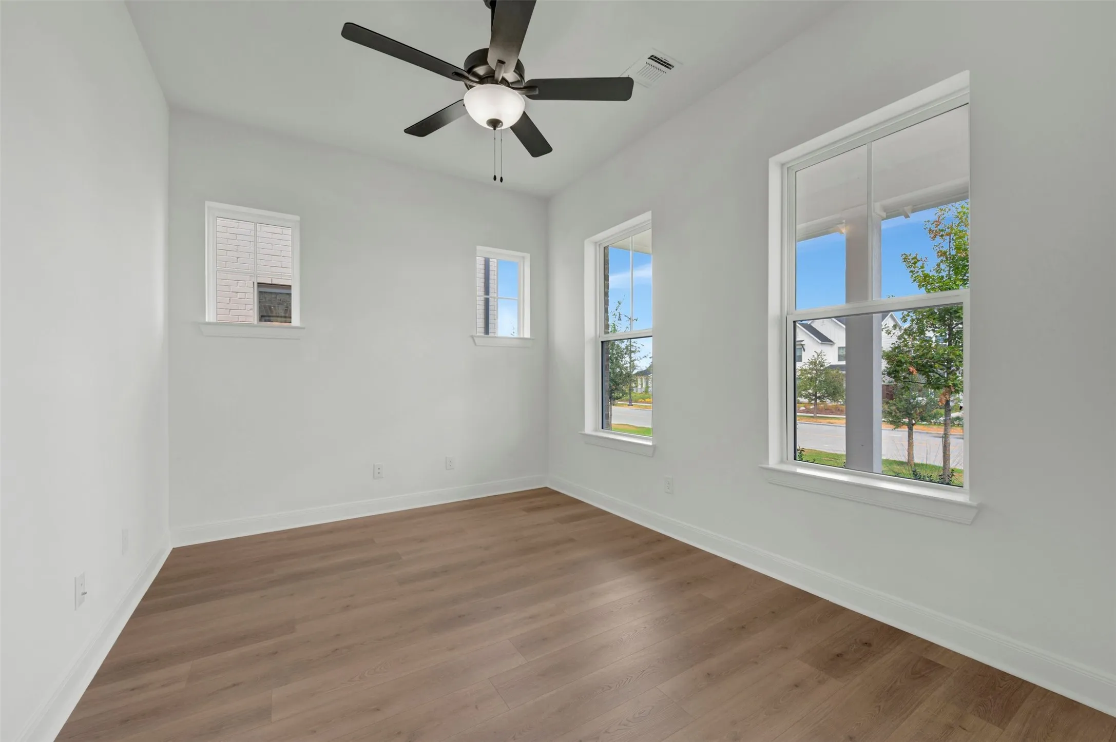 Bright and airy bedroom showcasing pristine white walls, engineered wood-finish flooring throughout, and abundant natural light from multiple large windows