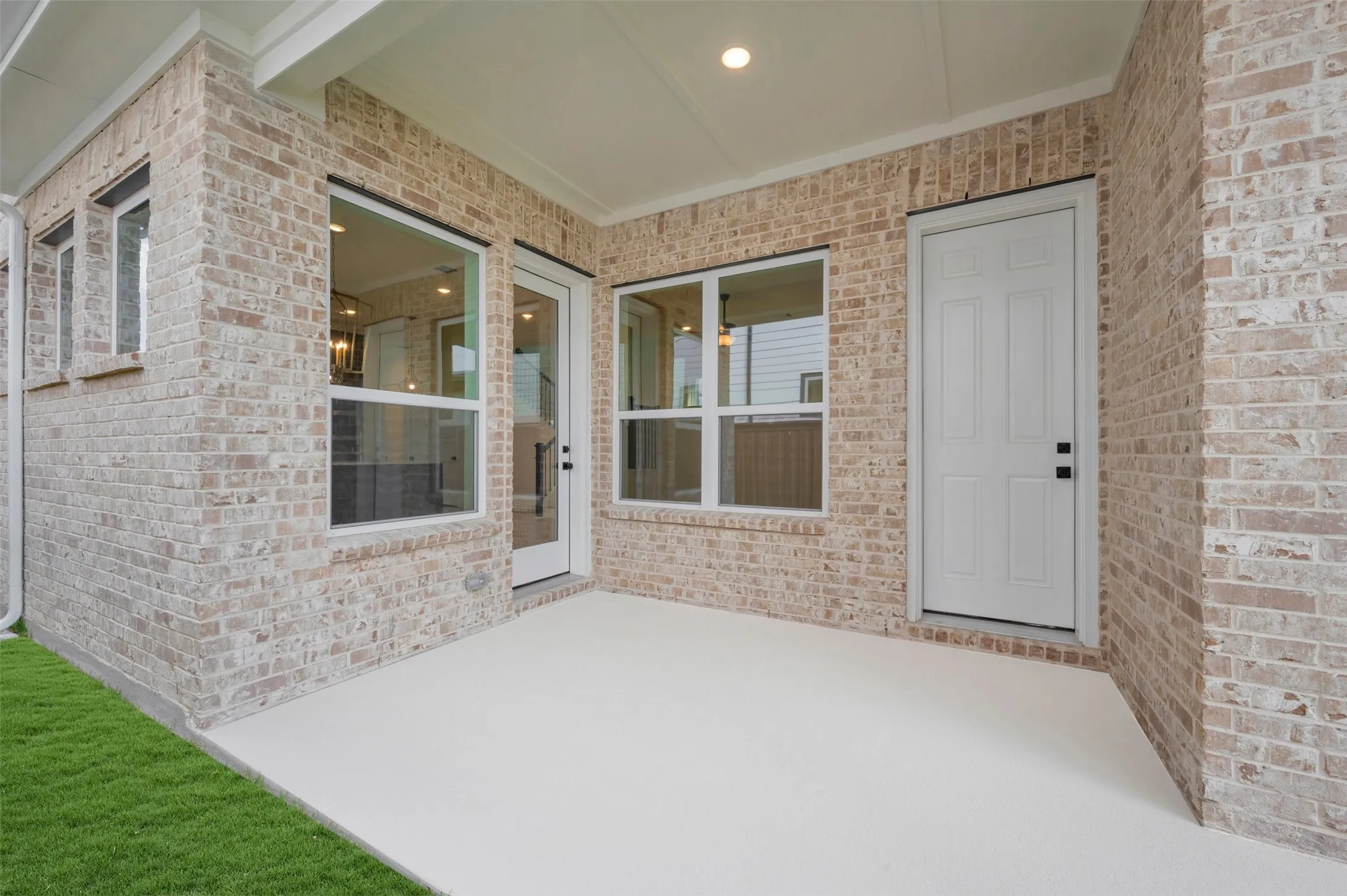 Covered patio with brick facade, concrete flooring, and multiple window and door access points