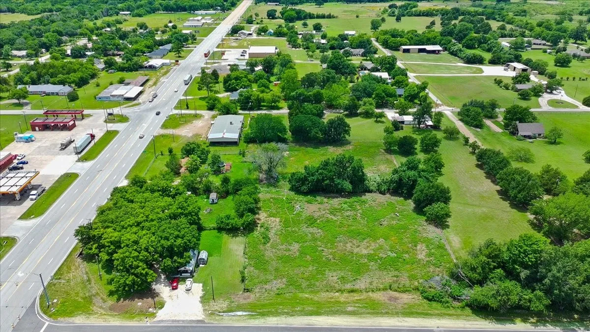 Expansive open lot featuring a clear building site, mature trees, and direct frontage on a paved road