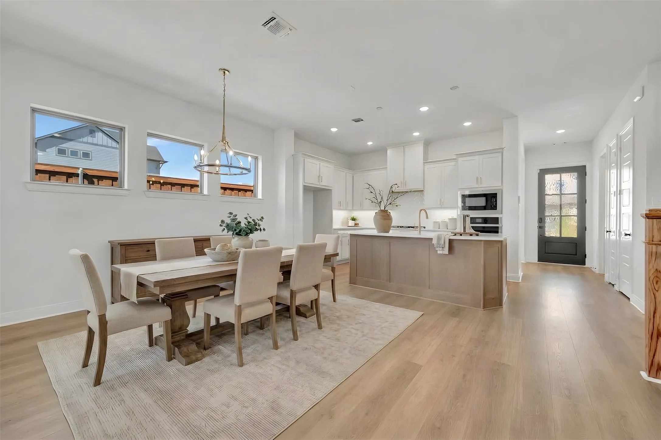 Open-concept living area featuring light wood-finish flooring, recessed lighting, a modern chandelier, and multiple windows