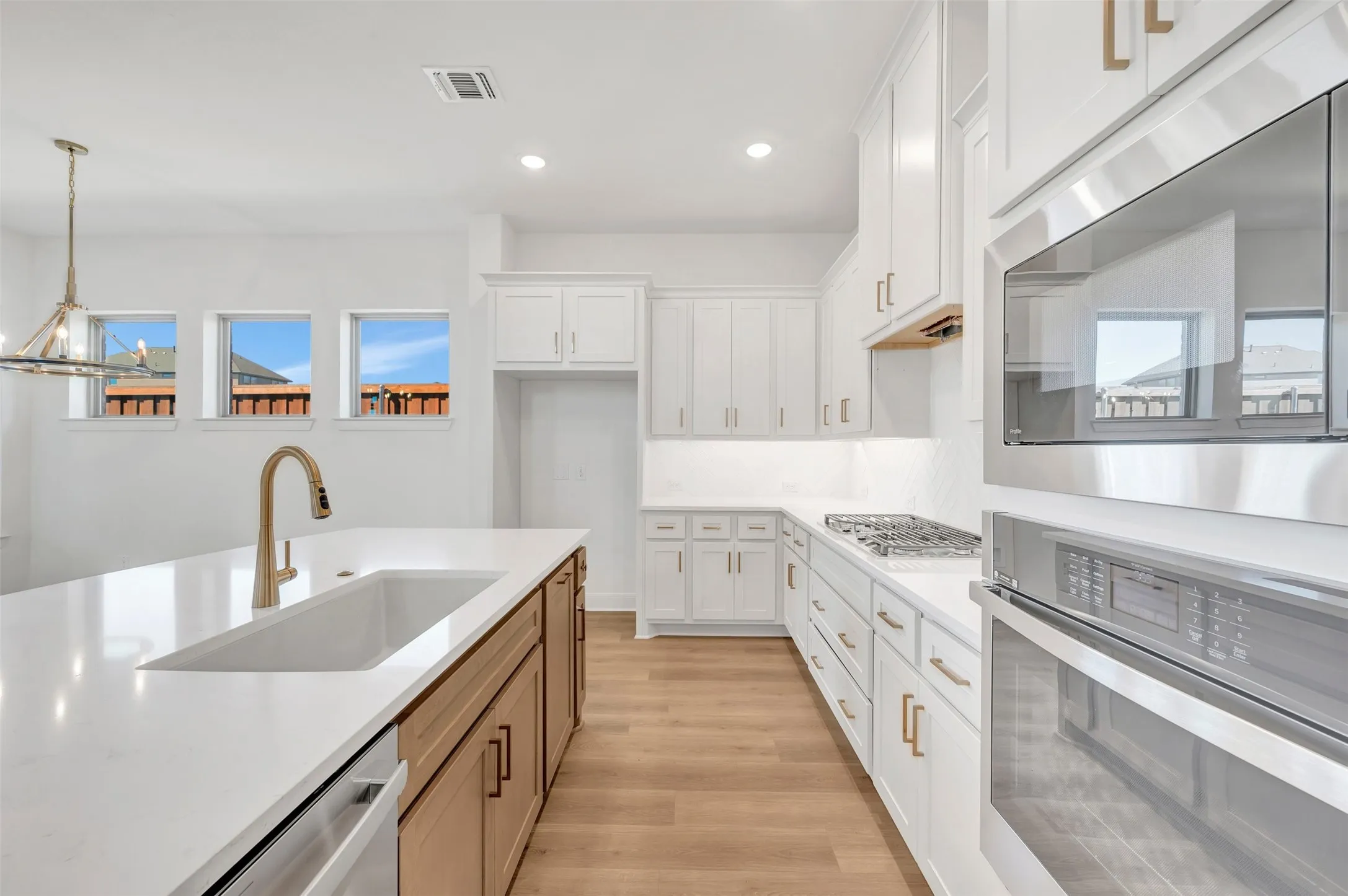 Kitchen featuring white cabinetry, light wood-finish flooring, stainless steel appliances, and a central island with an undermount sink and brass-finish faucet