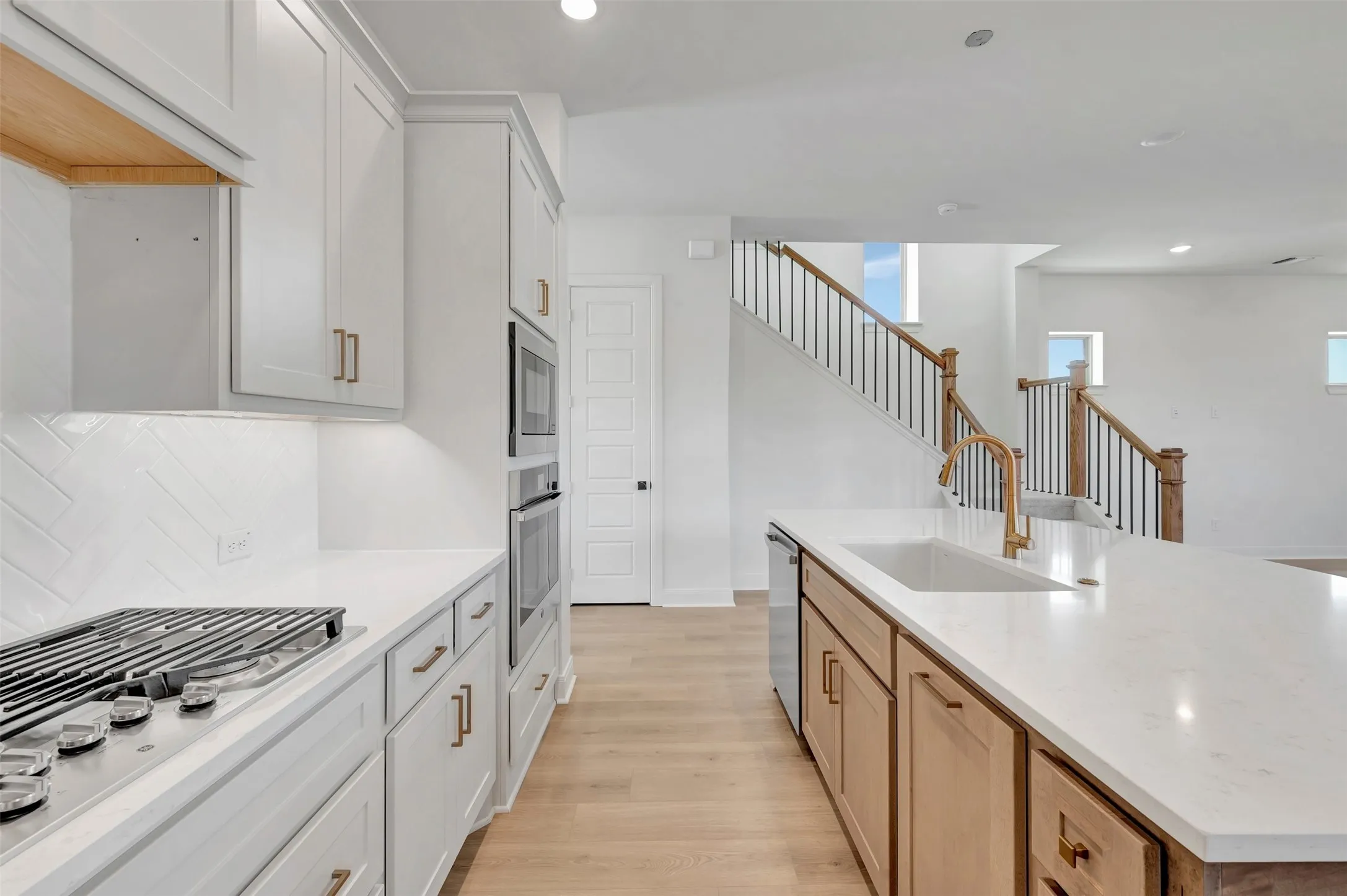 White kitchen cabinetry with a herringbone tile backsplash and stainless steel appliances