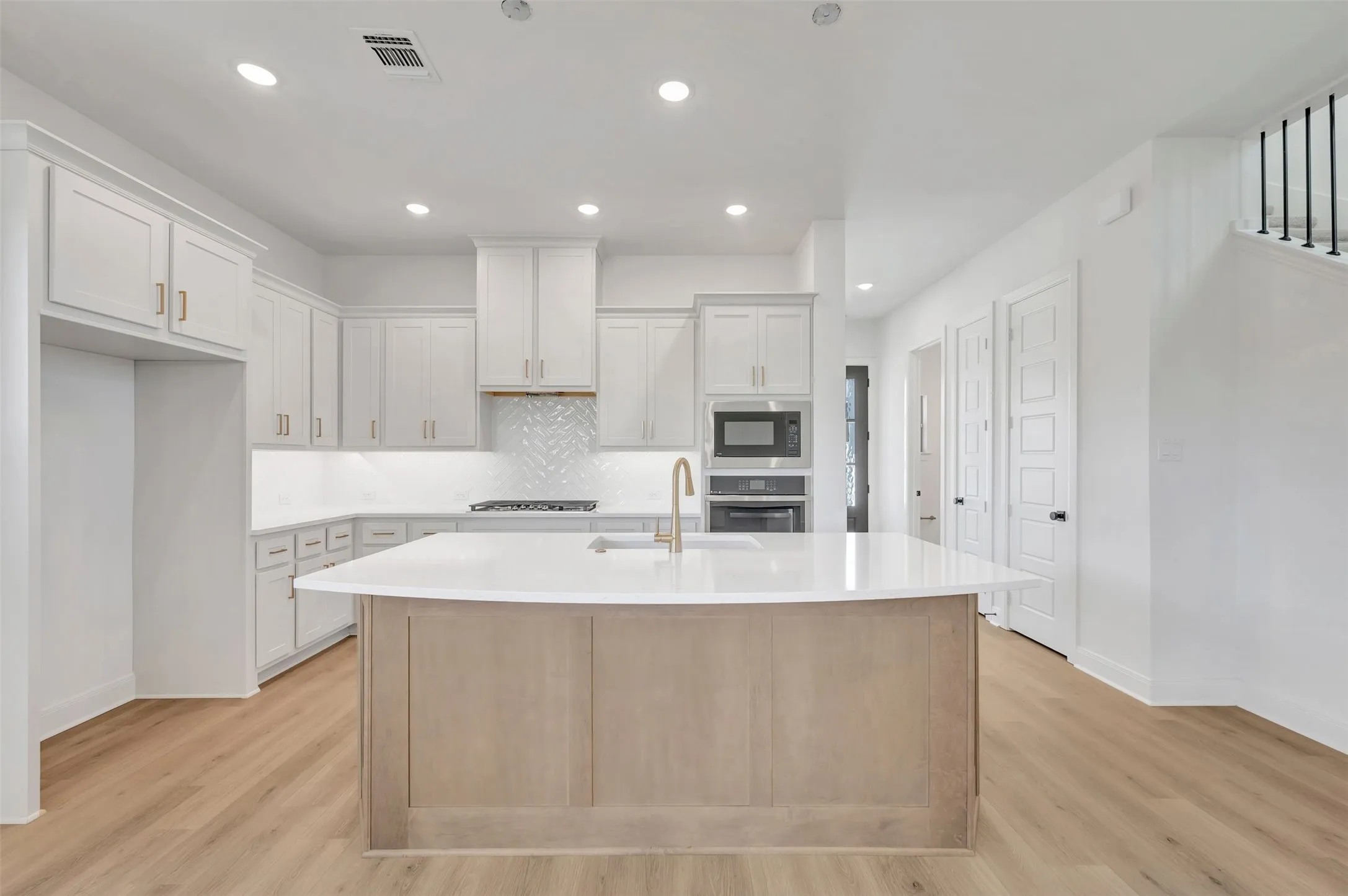 Gourmet kitchen with white cabinetry, light-toned wood-finish flooring, a large island with a light countertop, and integrated stainless-steel appliances