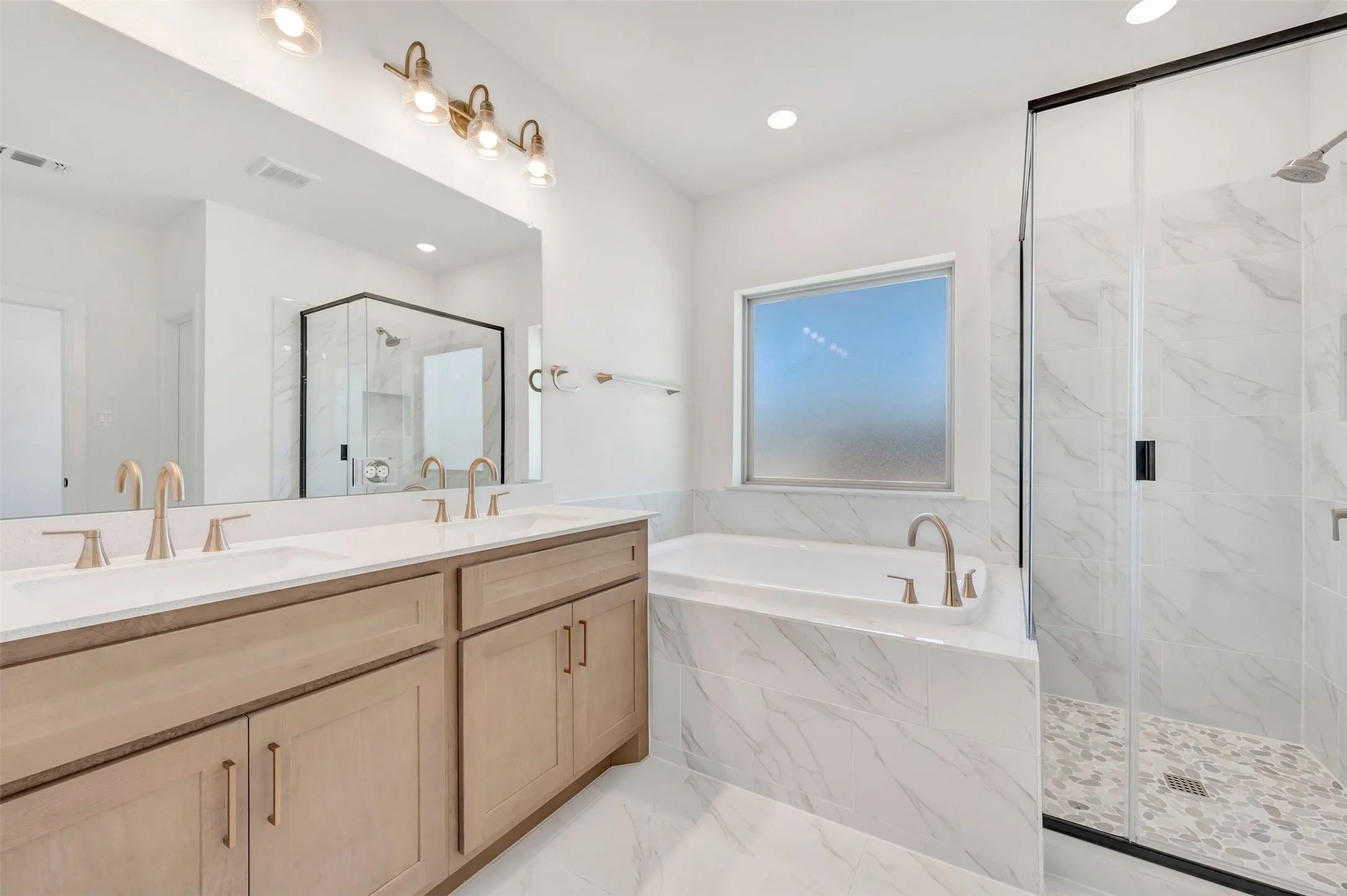 Dual vanity with light wood-finish cabinetry, white countertop, and gold-finish fixtures
