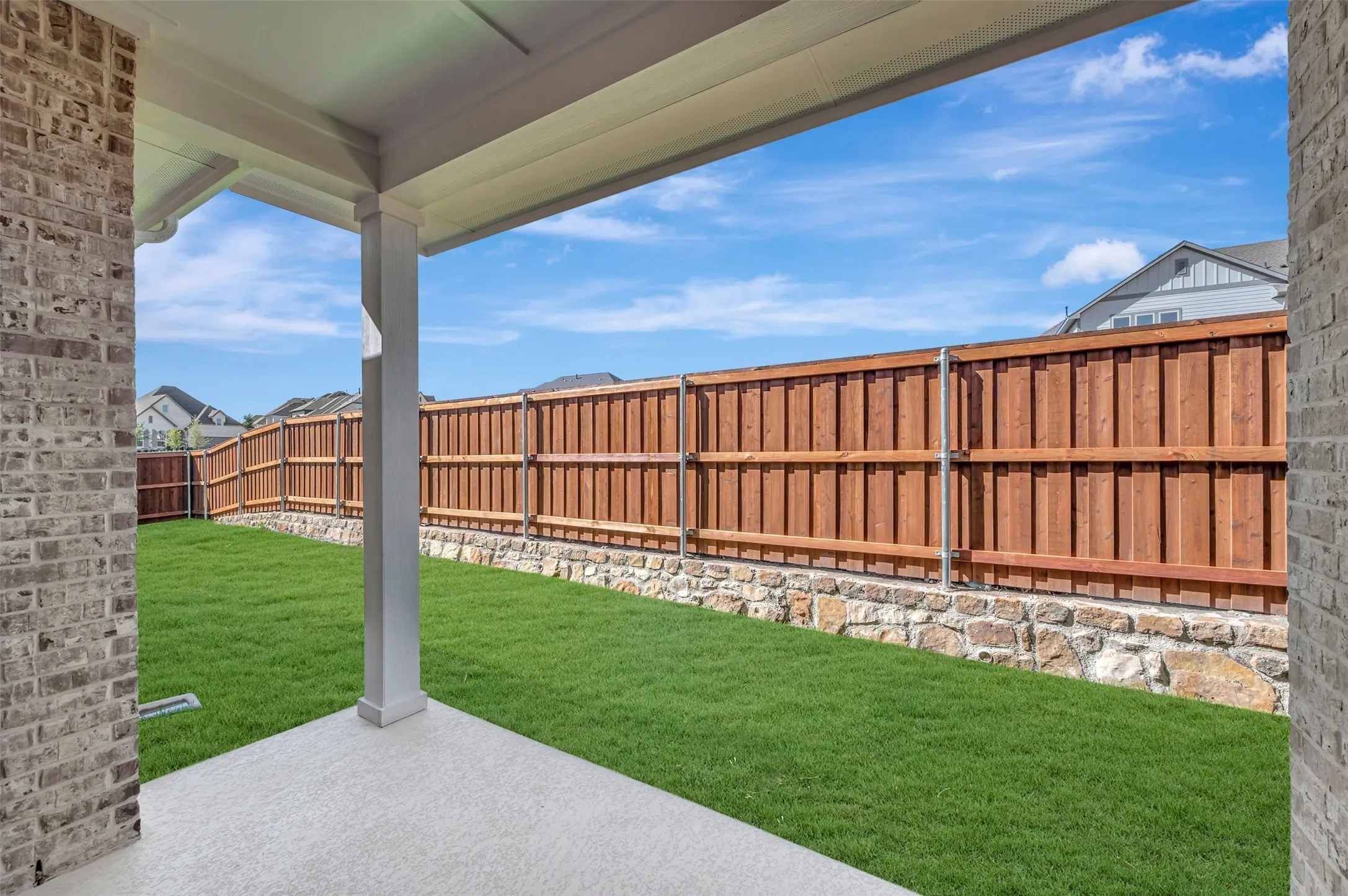 Covered patio with a concrete surface, expansive lawn, and wood privacy fencing atop a stone retaining wall