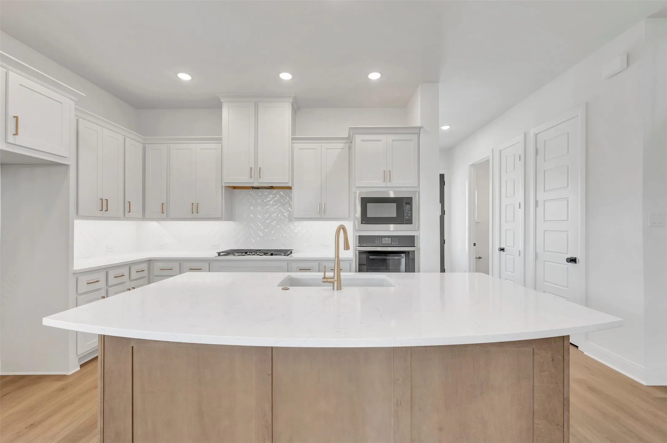 Modern kitchen featuring white cabinetry, a large center island with a built-in sink, stainless steel appliances, and wood-finish flooring