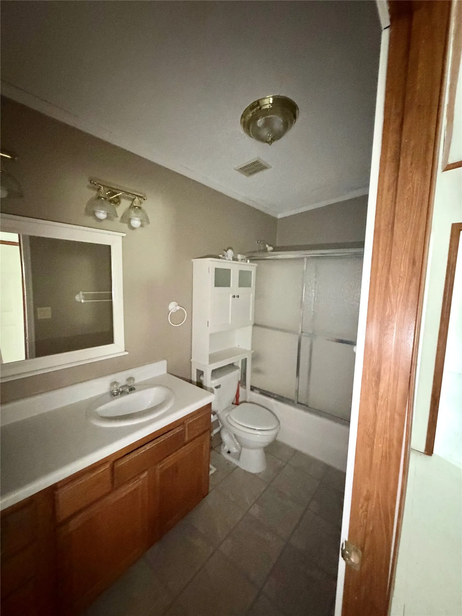 Bathroom featuring a wood-finish vanity with a white countertop and integrated sink, a rectangular framed mirror, and a full-size bathtub with a sliding glass door
