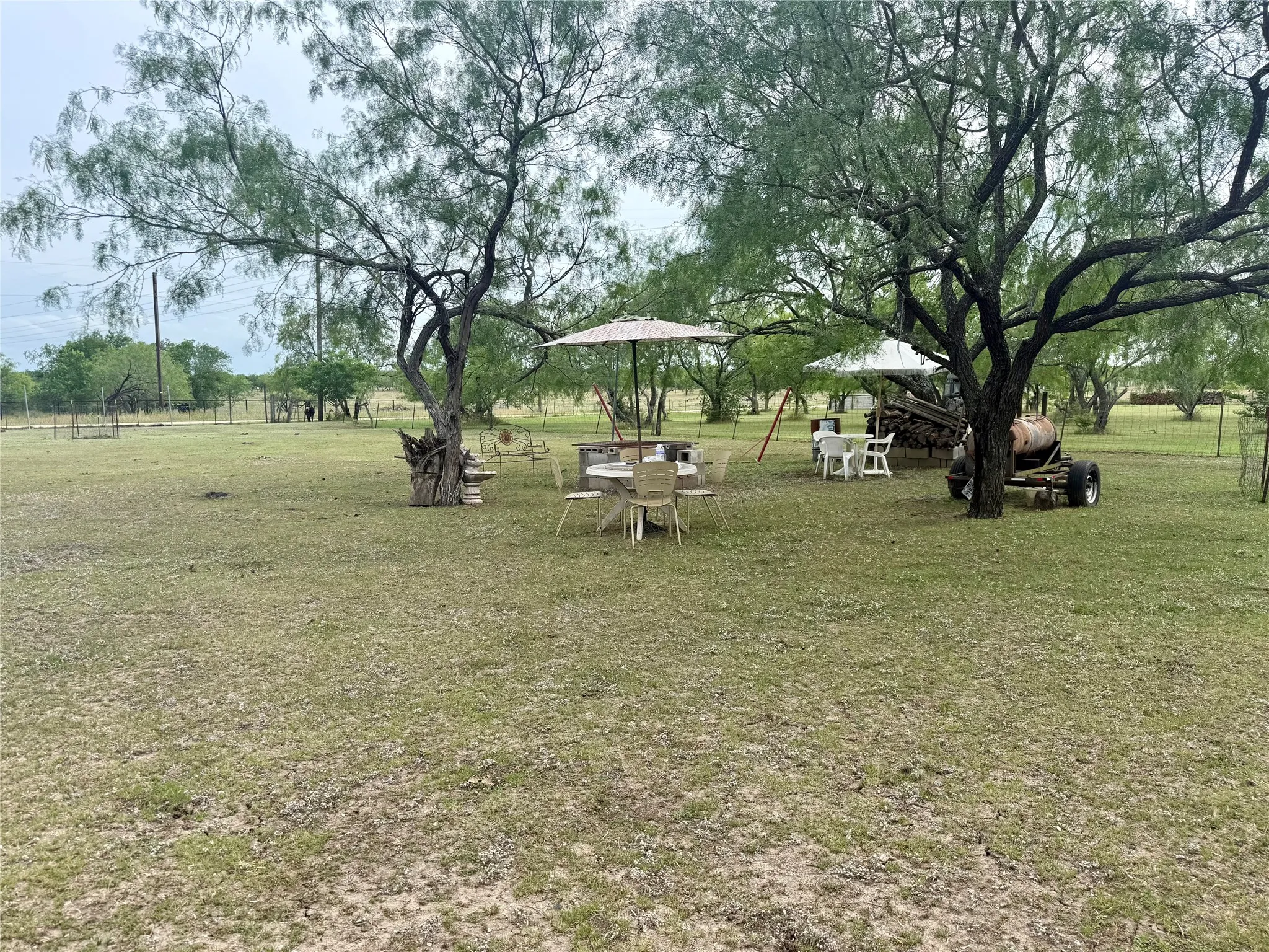 Expansive outdoor space featuring mature trees, a large grassy area, and a rustic smoker