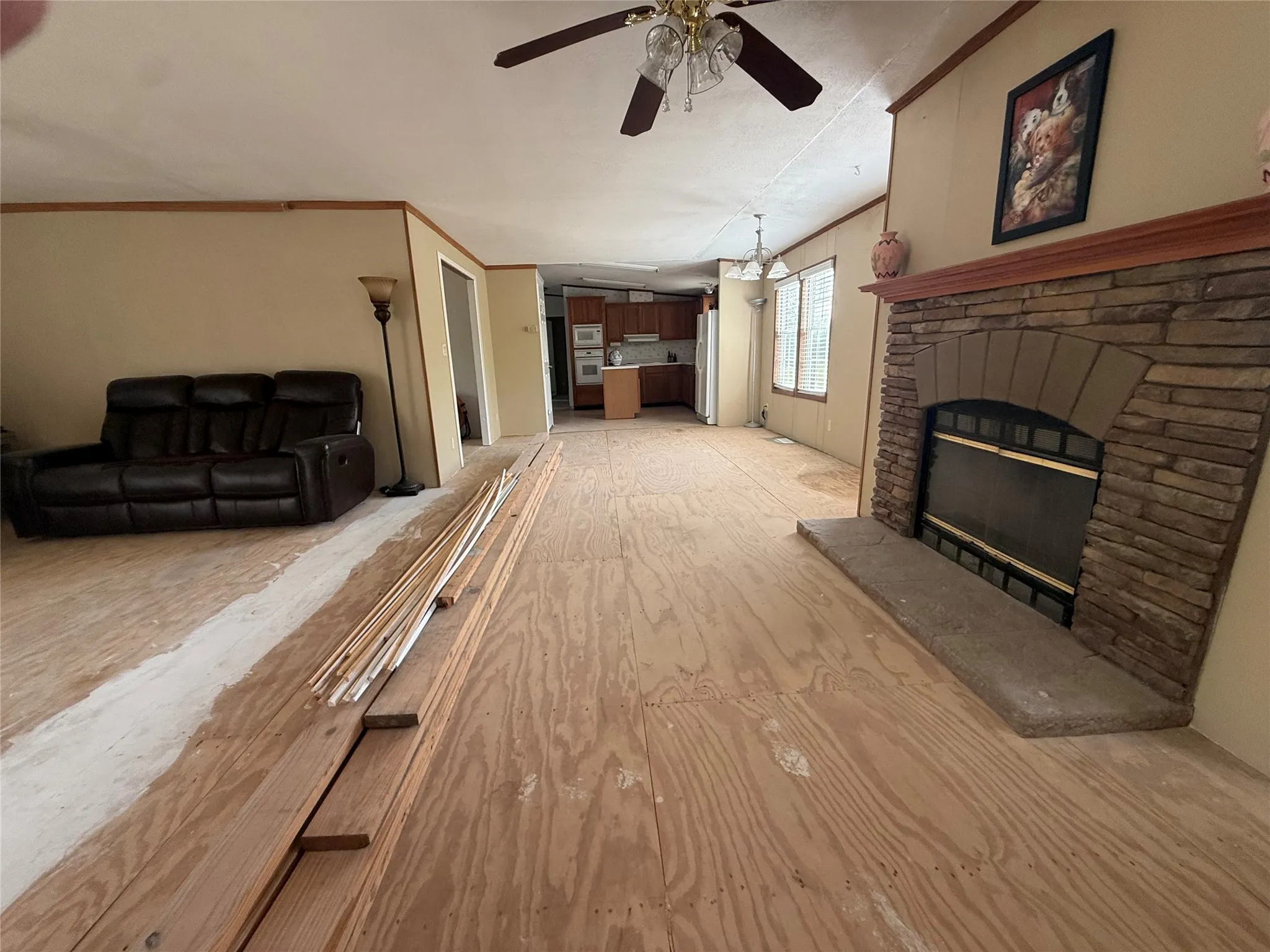 Central living area featuring a stone-clad fireplace with a hearth, plywood subflooring, and a ceiling fan with integrated lighting
