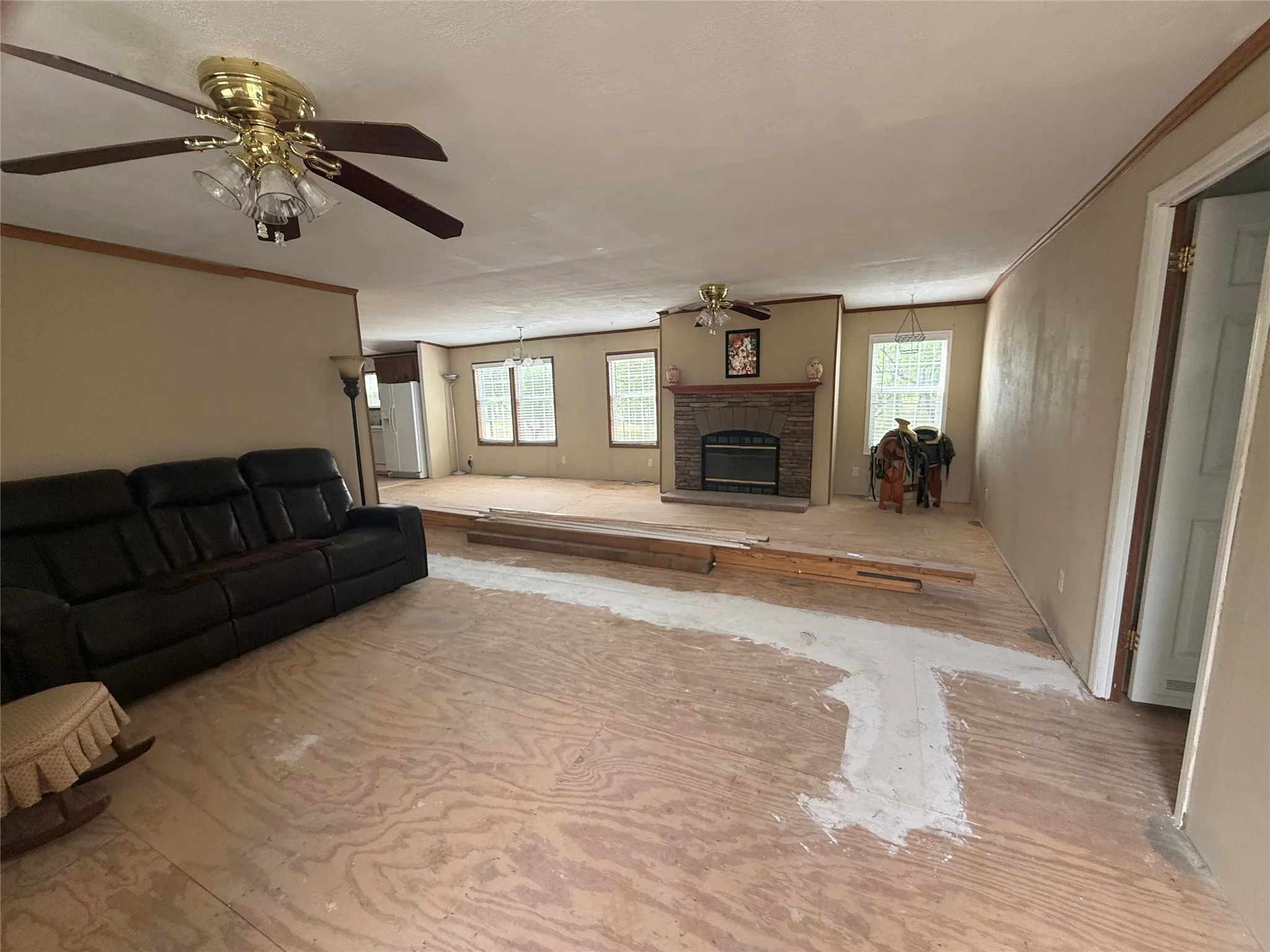 Living area featuring an integrated fireplace with a stone surround, a ceiling fan with light fixture, and multiple windows providing natural light