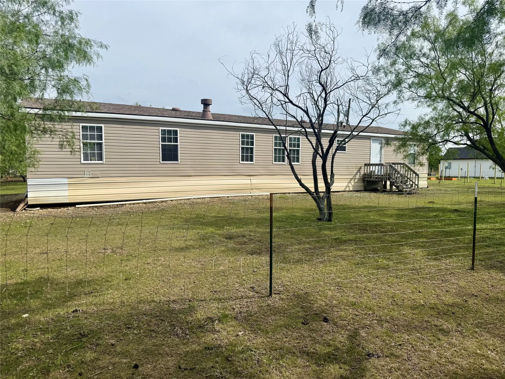 Single-story residence featuring tan siding and multiple windows, set on a grassy lot