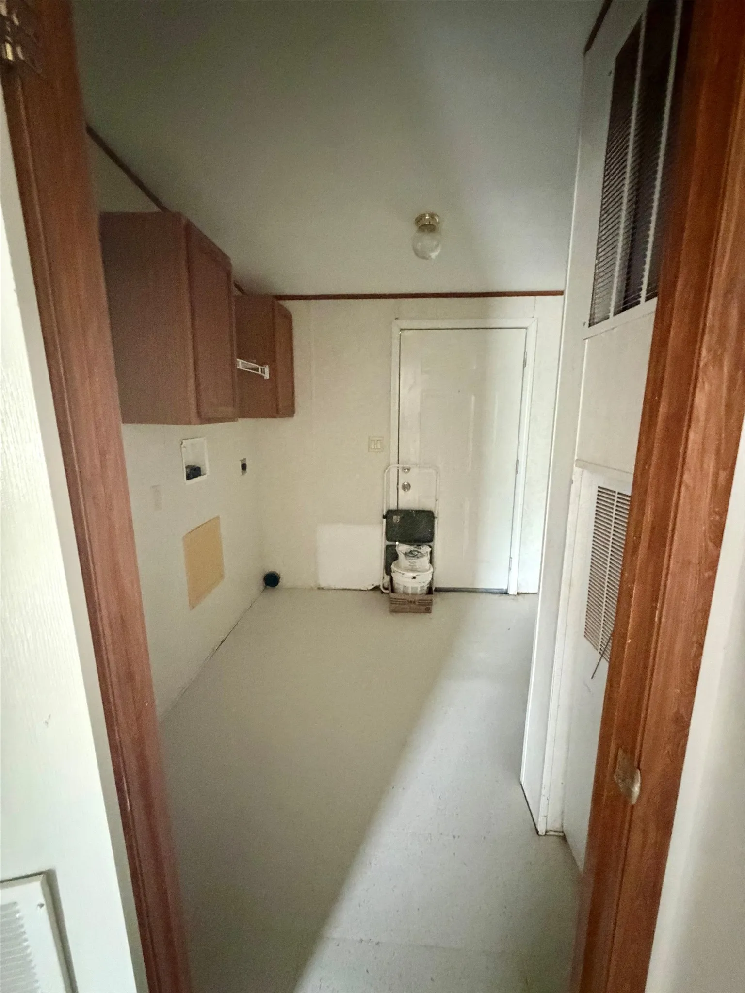 Utility area featuring overhead cabinetry, wall-mounted air vents, a white door, and light-colored flooring