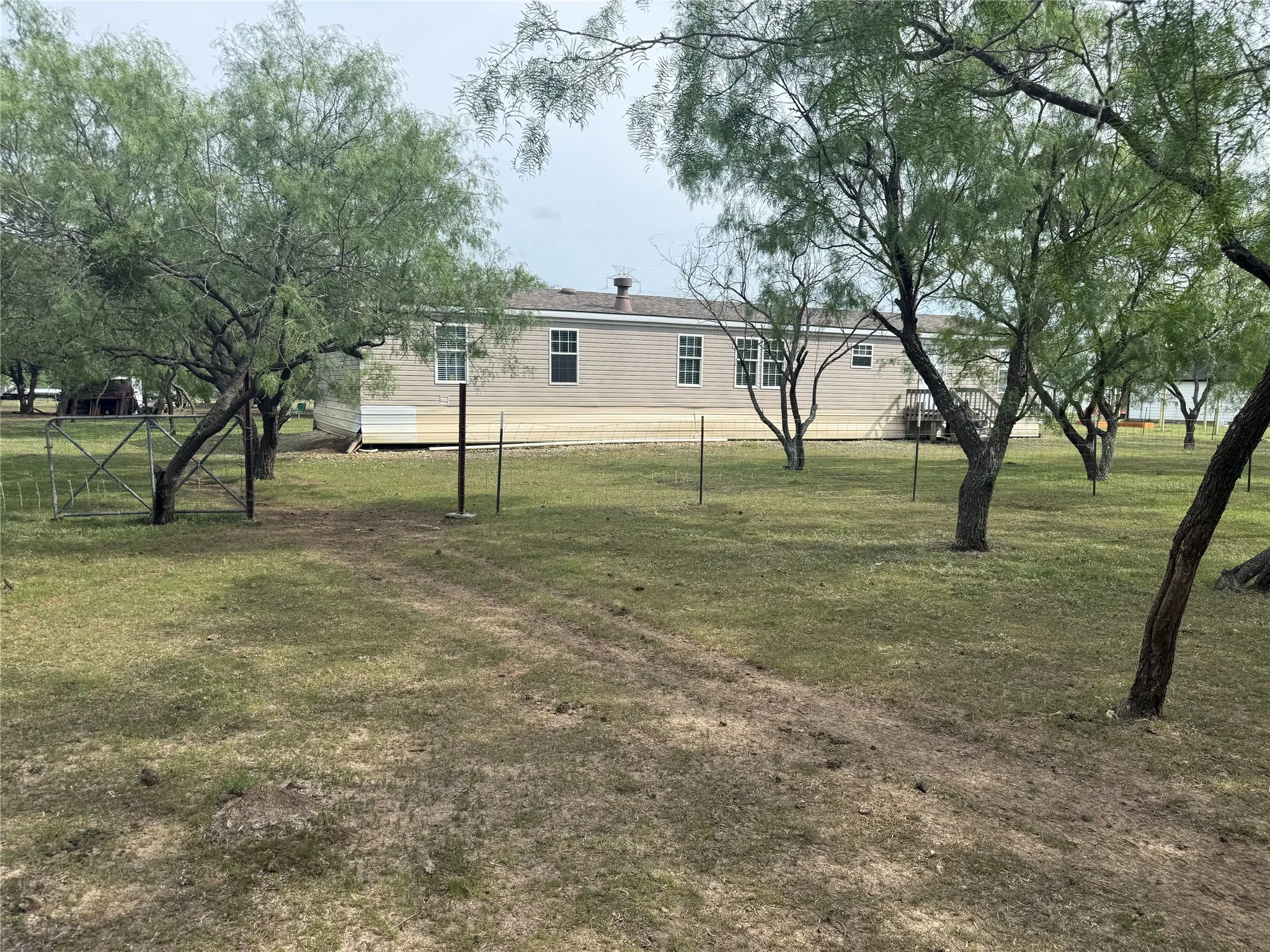 Expansive lot featuring a single-story residence with light-colored siding, multiple windows, and a shingled roof