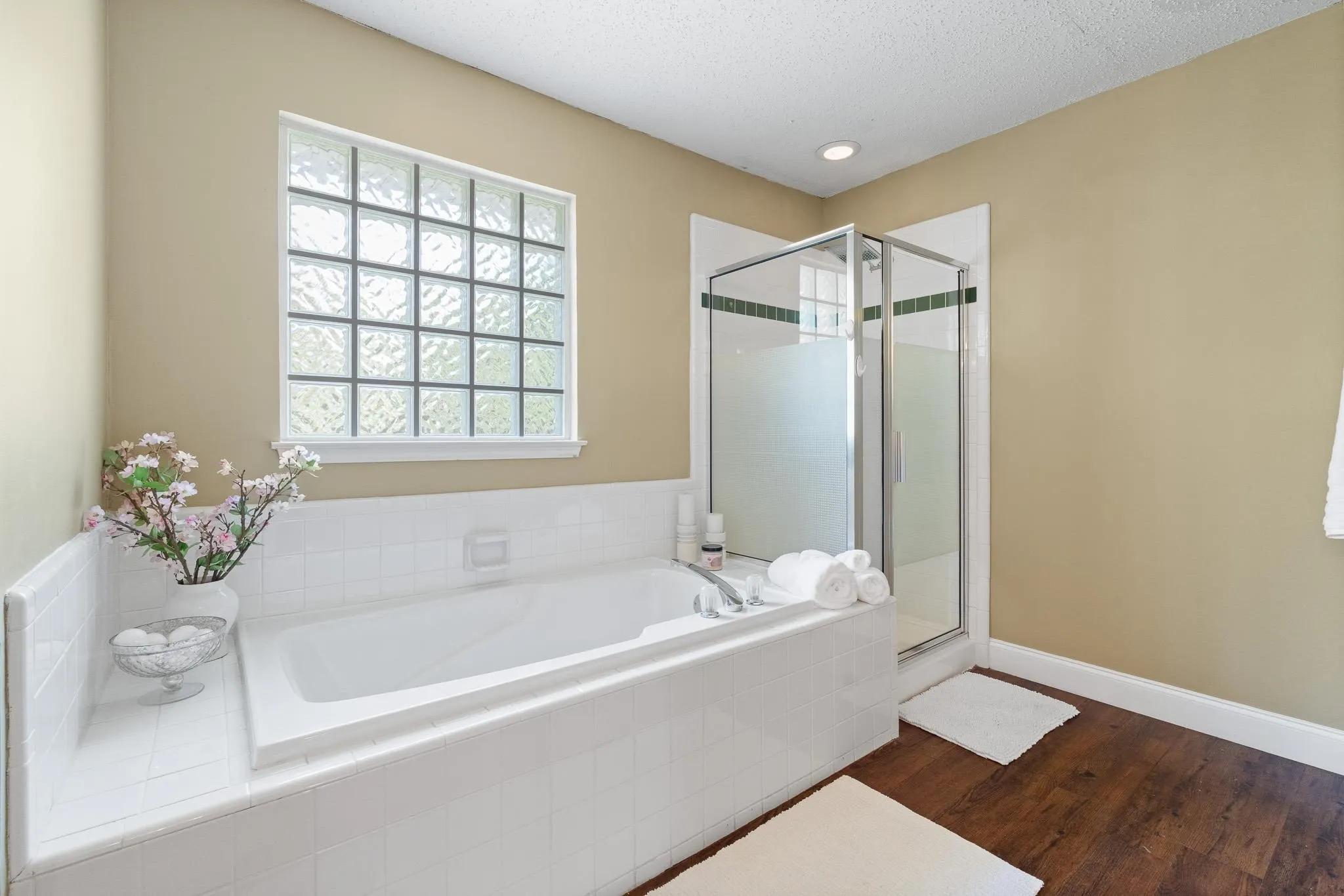 Deep-soaking tub with white tile surround, glass block window, and adjacent glass-enclosed shower with frosted paneling