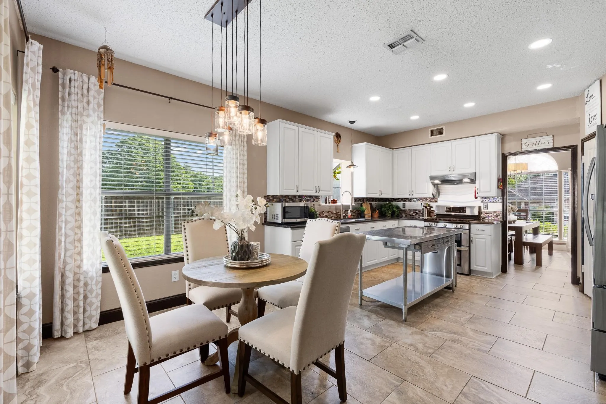 Spacious kitchen and dining area featuring white cabinetry, a stainless steel kitchen island, and a contemporary chandelier