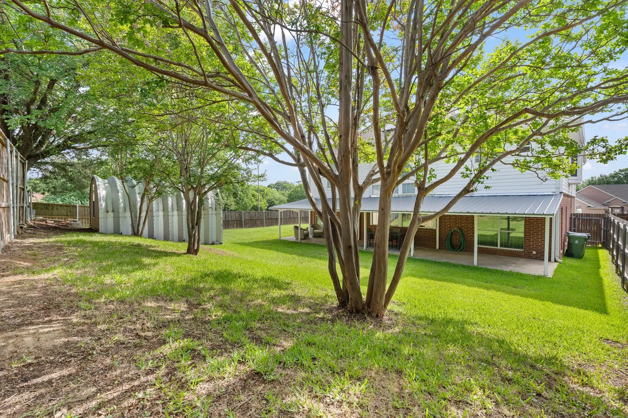 Expansive backyard featuring a mature tree, manicured lawn, and a covered patio with brick columns