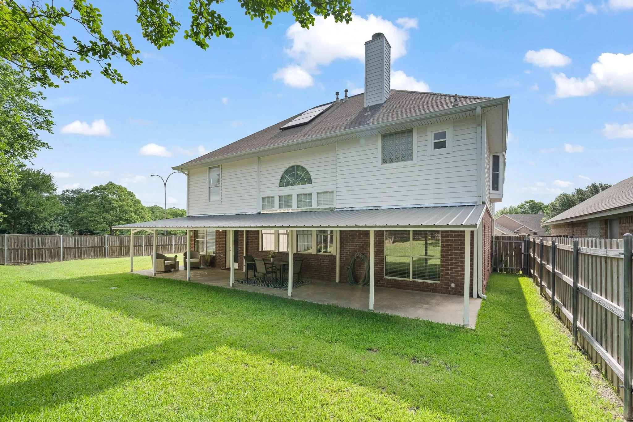 Expansive green yard featuring a covered patio, white siding, and a brick exterior