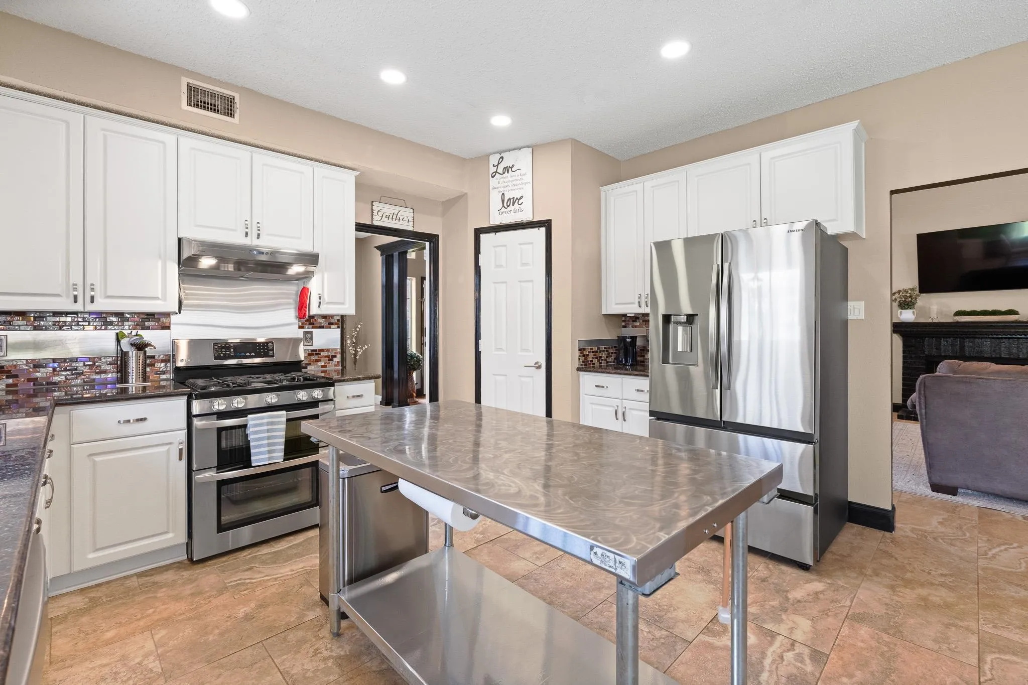 Kitchen featuring a stainless steel range, coordinating stainless steel refrigerator, white cabinetry, dark countertops, and a full tile backsplash