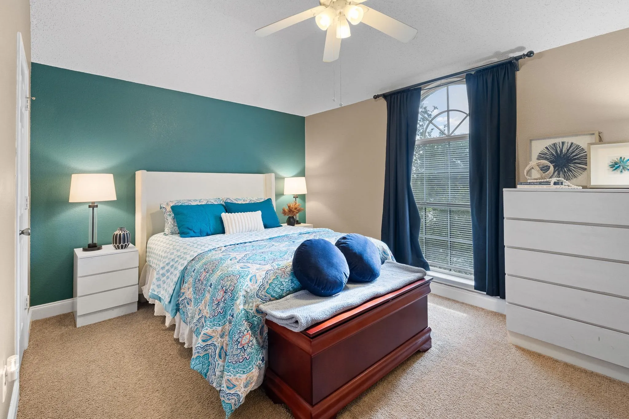 Carpeted bedroom featuring an arched window, a ceiling fan, and a painted accent wall