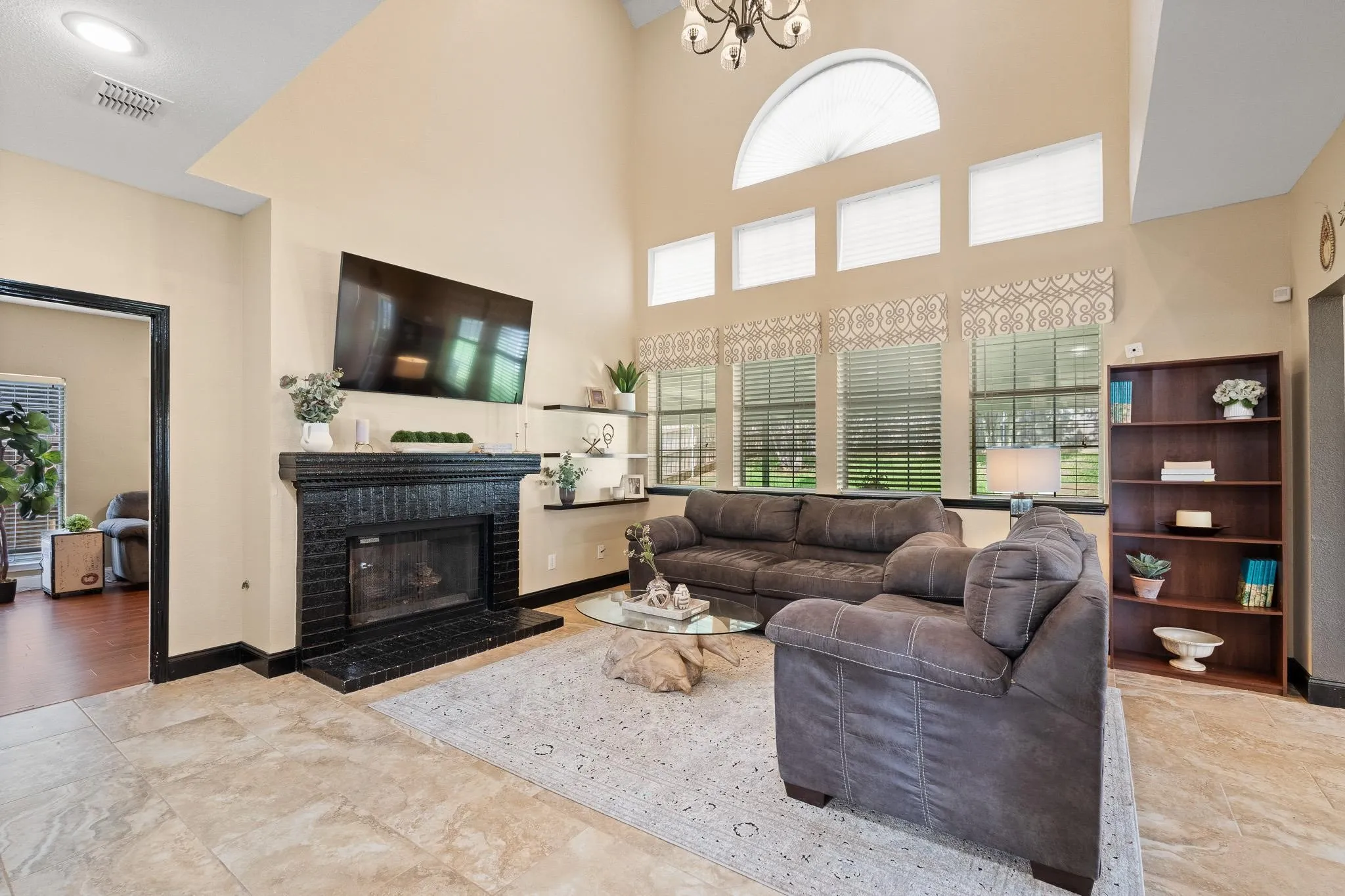 Spacious living area featuring a vaulted ceiling, a black brick fireplace, multiple windows with arched transom above, and light-toned tile flooring