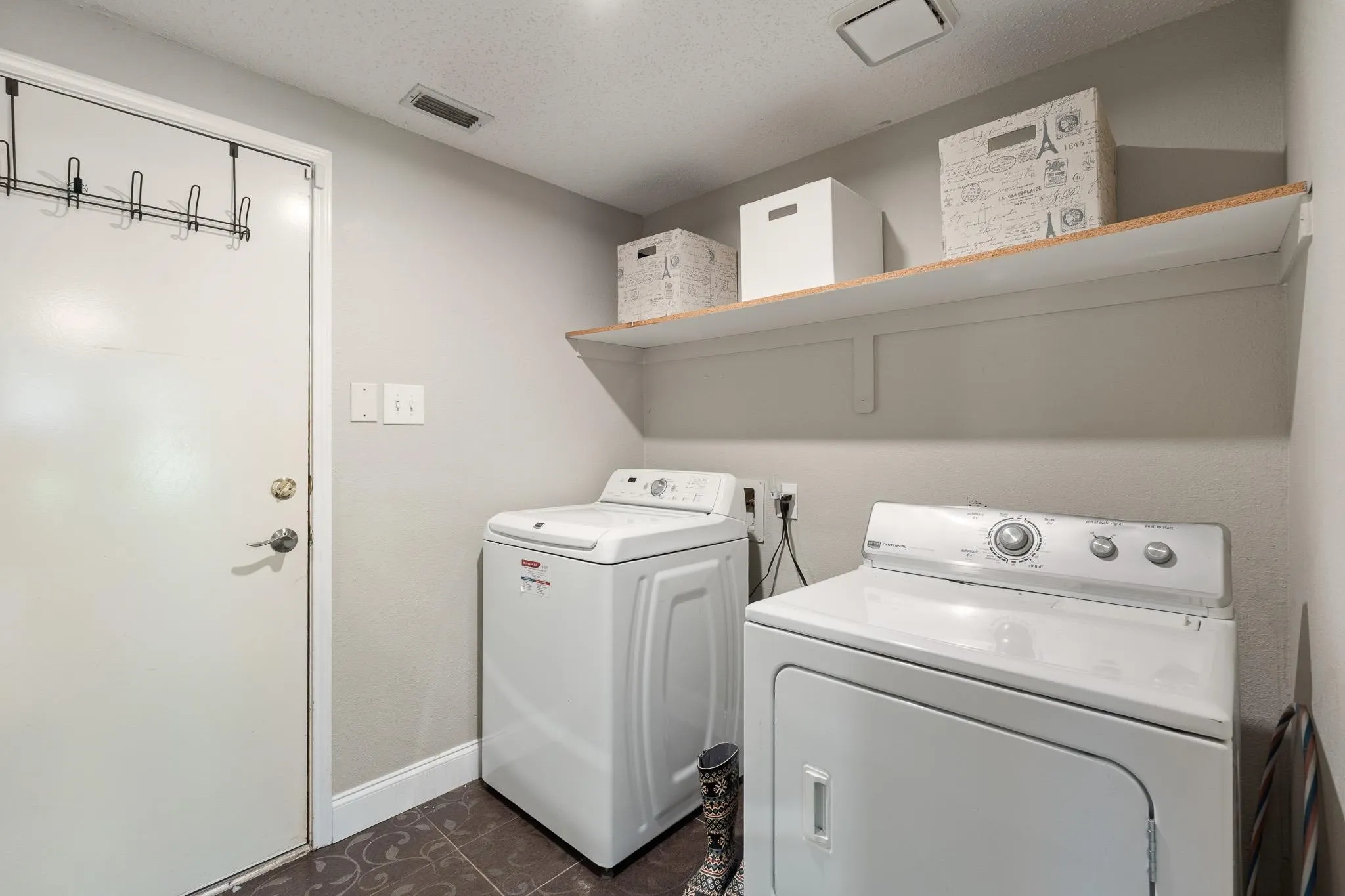 Dedicated utility space featuring a washer and dryer, patterned floor tile, and an elevated wood-finish shelf