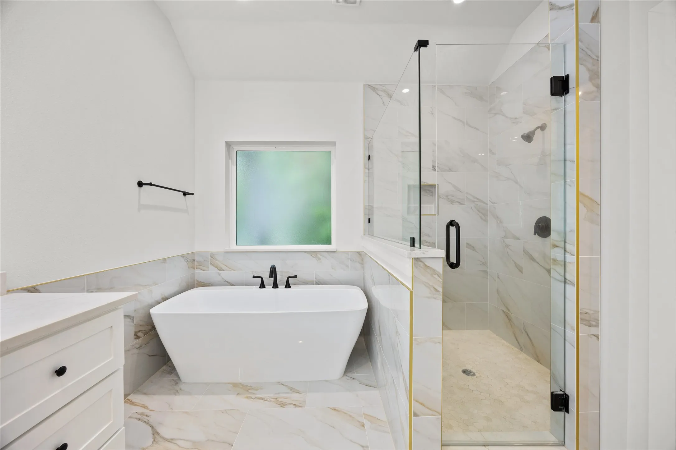 Spacious bathroom featuring a freestanding soaking tub, a frameless glass shower enclosure, and large format marble-look tile flooring