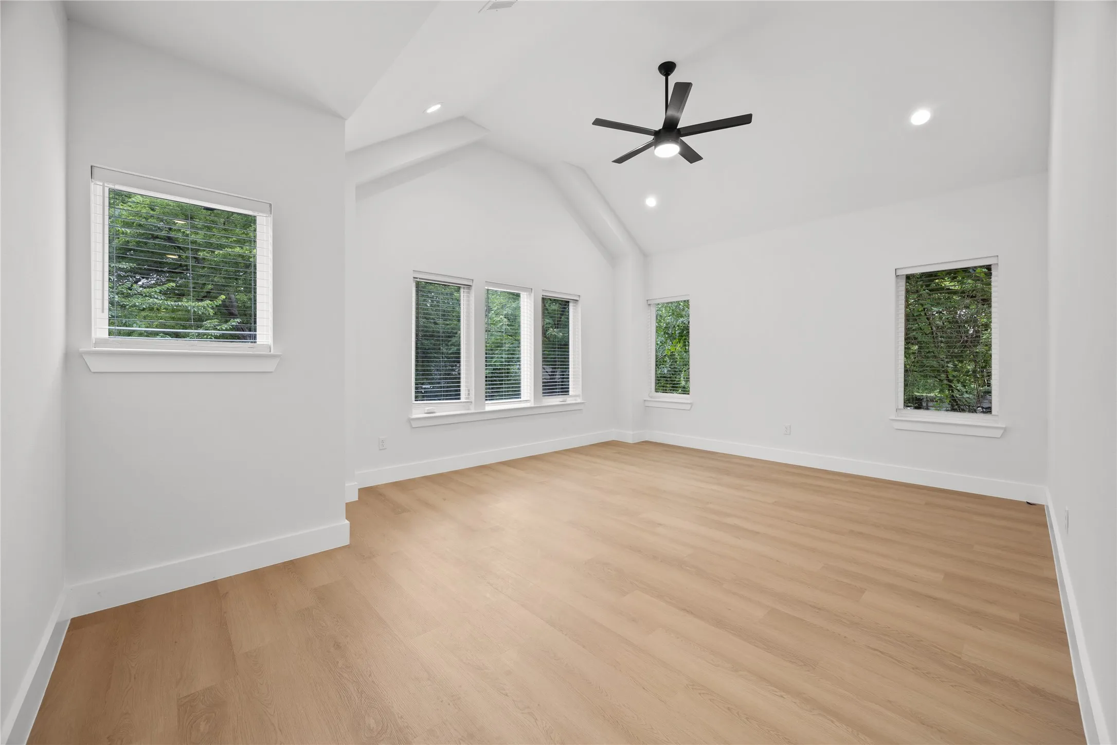 Spacious room featuring vaulted ceilings, a contemporary ceiling fan, recessed lighting, wood-finish flooring, and multiple windows with white blinds