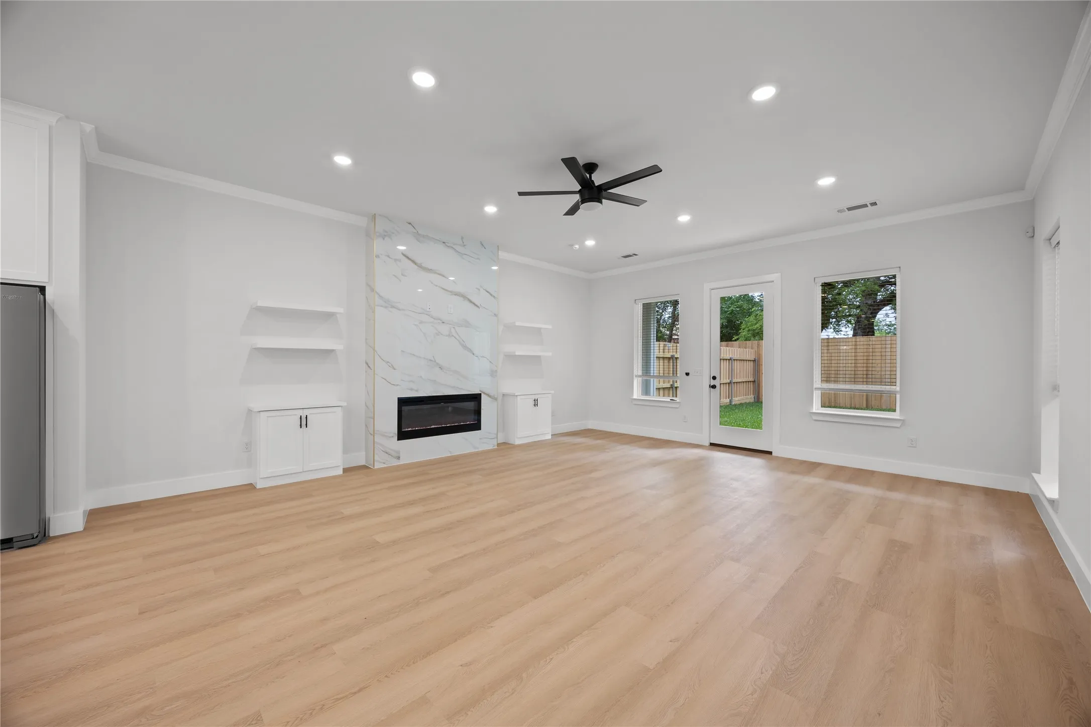 Spacious living area featuring wood-finish flooring, a contemporary fireplace with a marble-look surround, integrated shelving, recessed lighting, and a ceiling fan