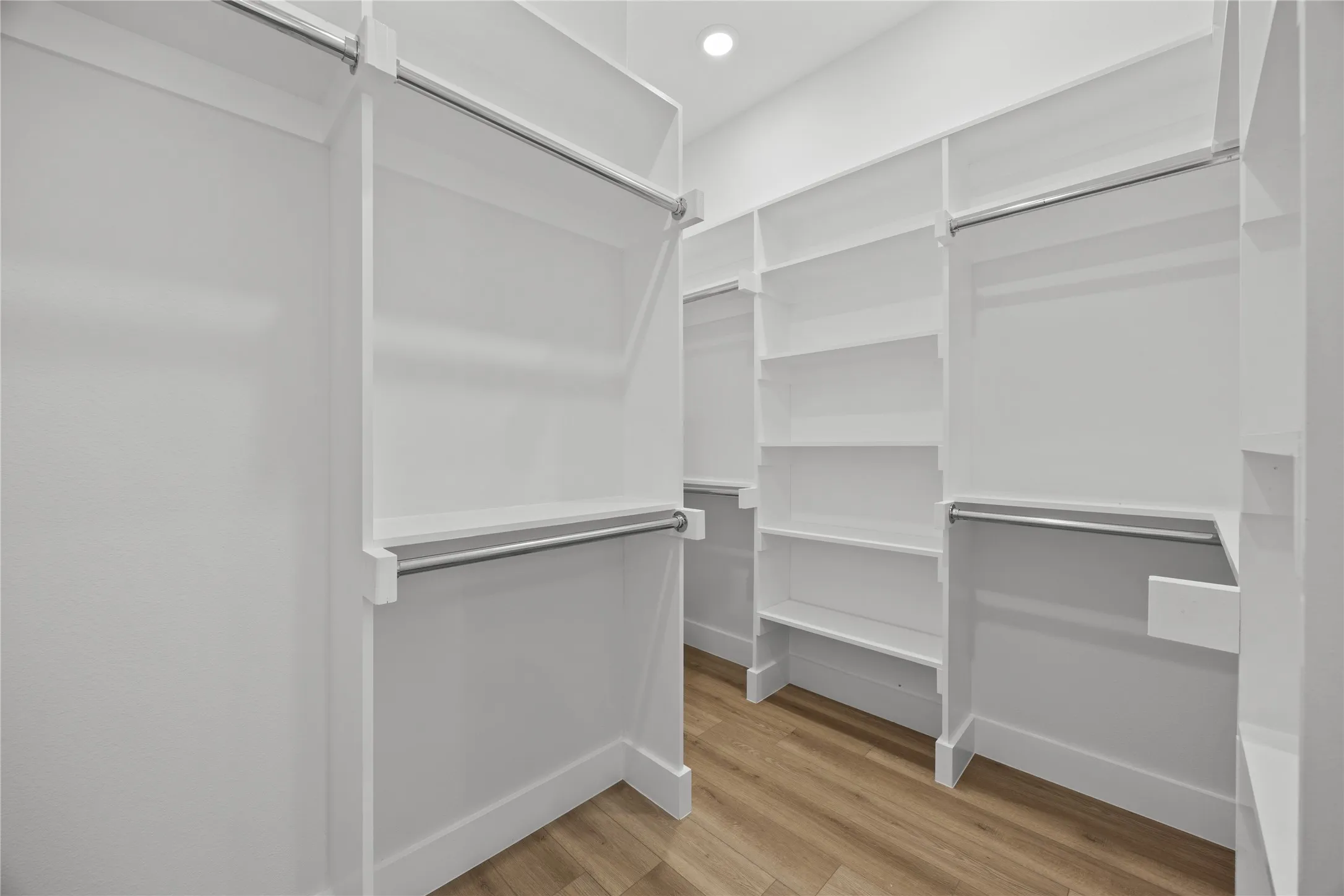 Spacious walk-in closet featuring extensive built-in shelving, multiple hanging rods, and wood-finish flooring