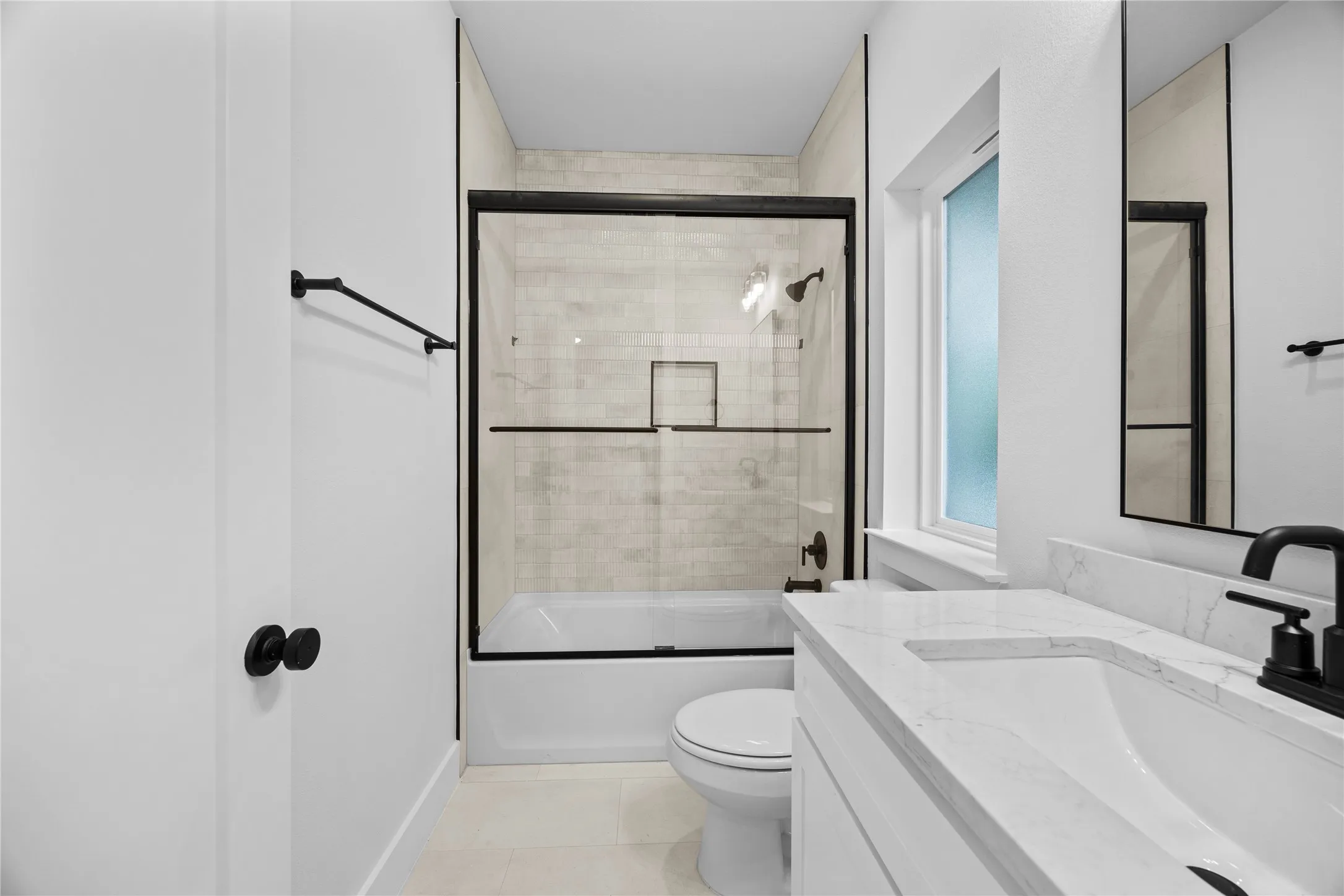 Bathroom featuring a white bathtub with a clear glass shower enclosure, matte black hardware, a single vanity with a white countertop, and a rectangular mirror