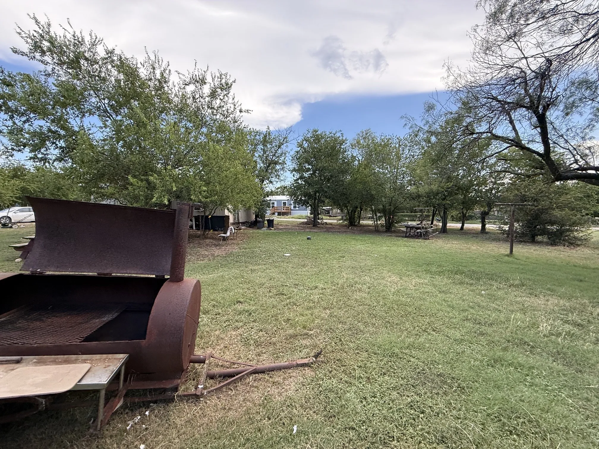 Expansive grassy yard area featuring mature trees and a picnic table
