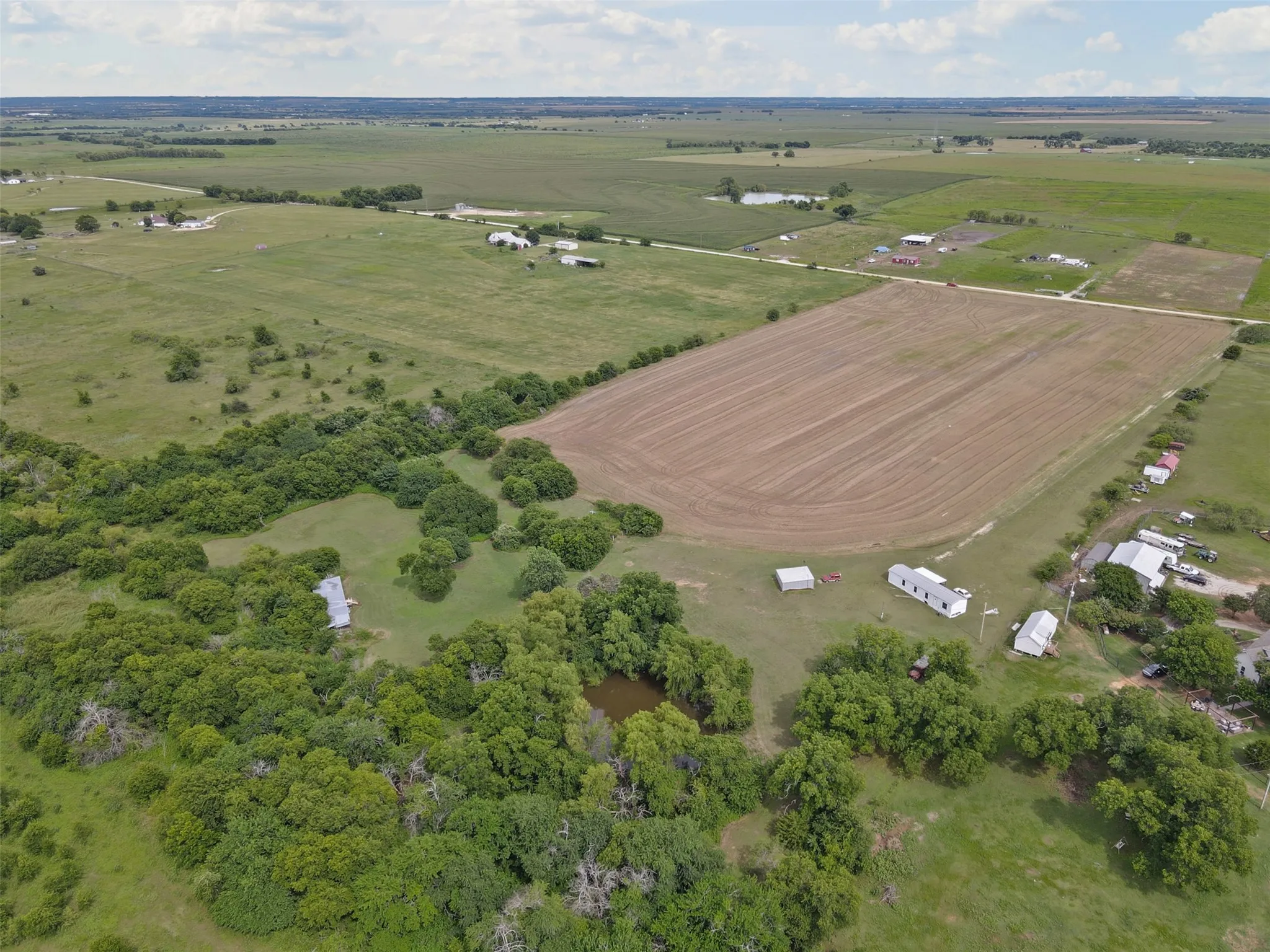 Extensive land parcel featuring a cultivated field, multiple structures, a pond, and mature tree coverage