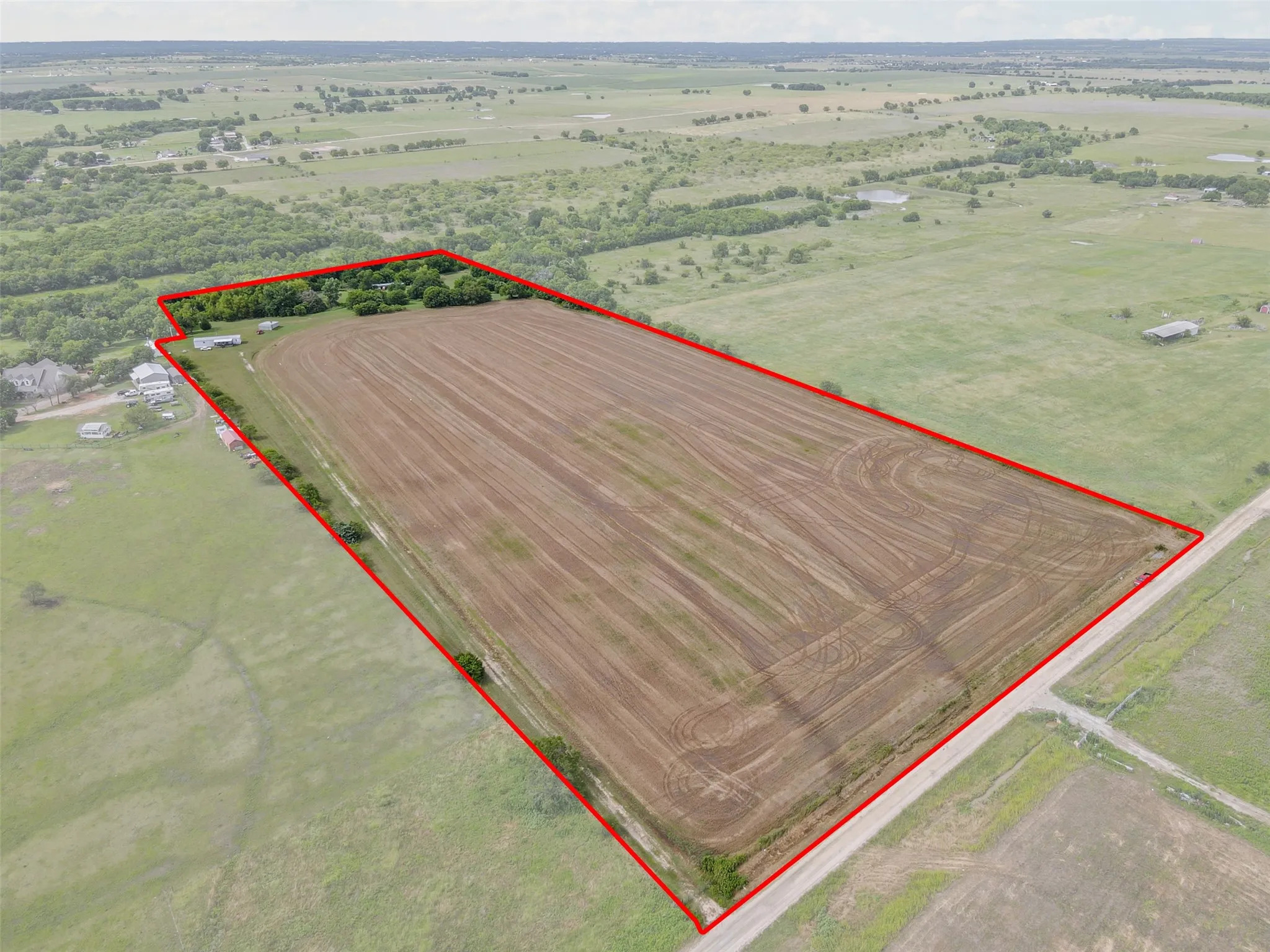 Expansive acreage featuring a tilled field, perimeter tree line, and a partial dirt road frontage