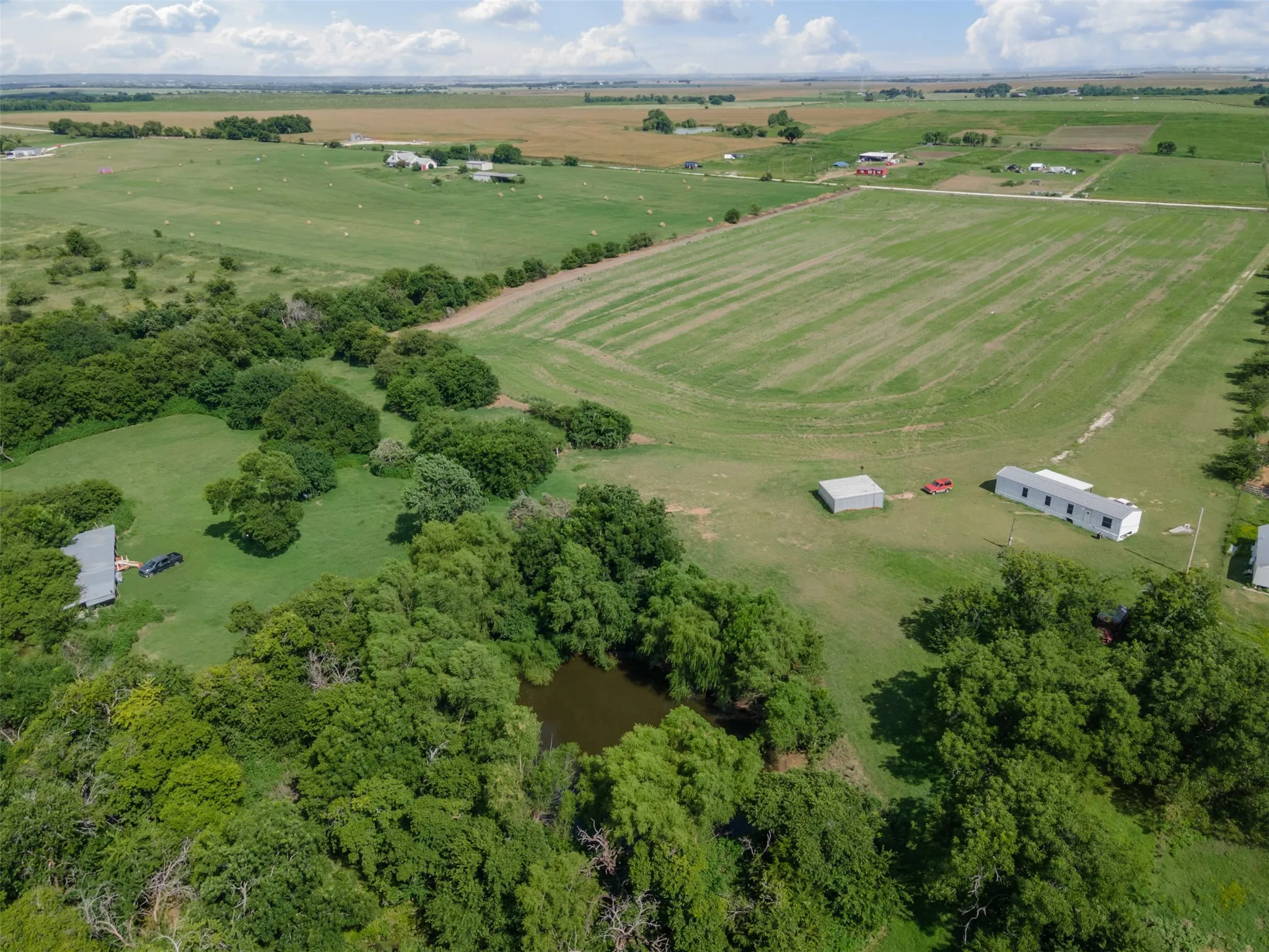 Expansive rural property featuring a large pond, extensive tree coverage, open fields, and multiple outbuildings