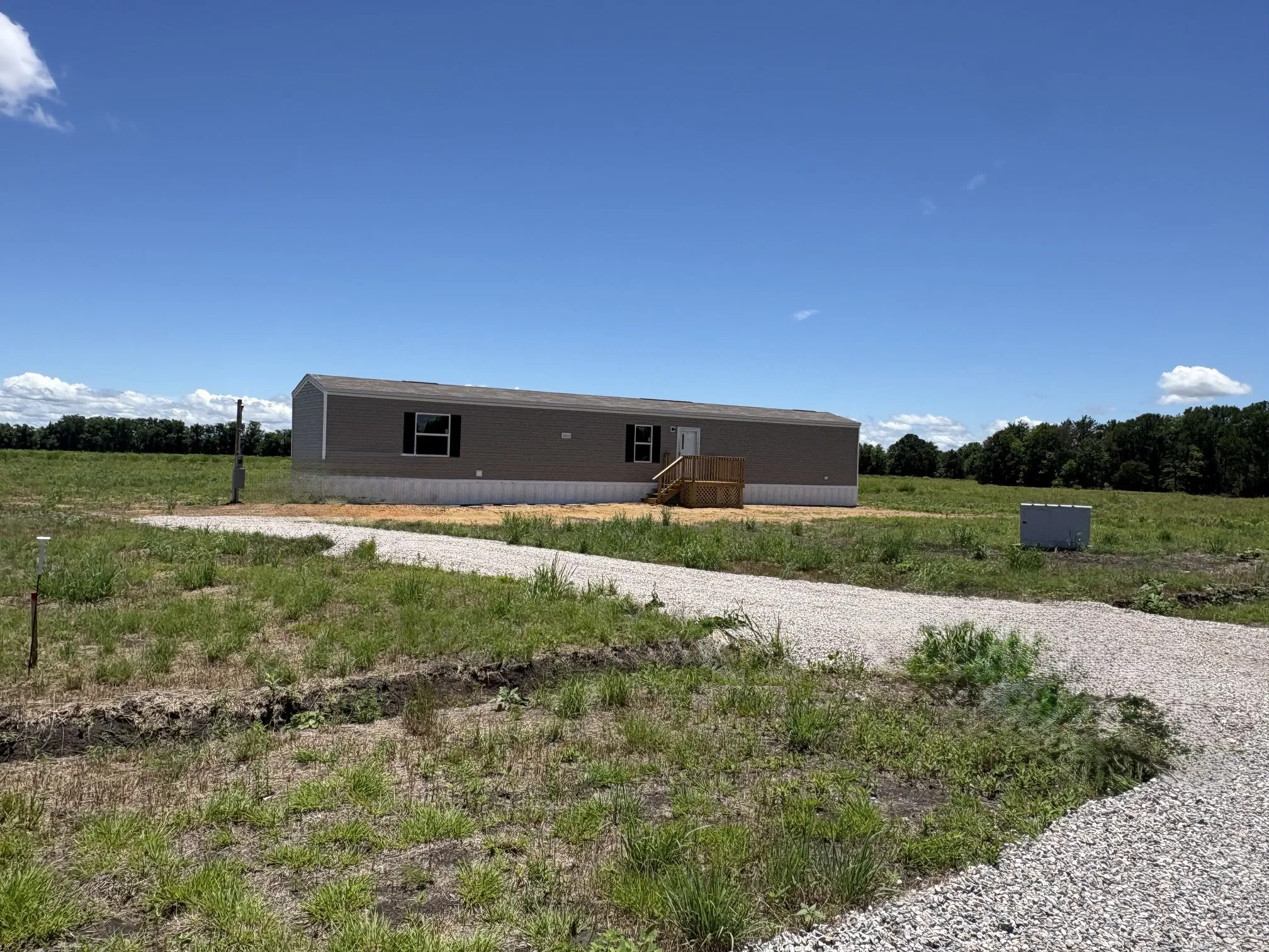 Manufactured home featuring neutral-toned siding, dark window shutters, and a light-colored foundation